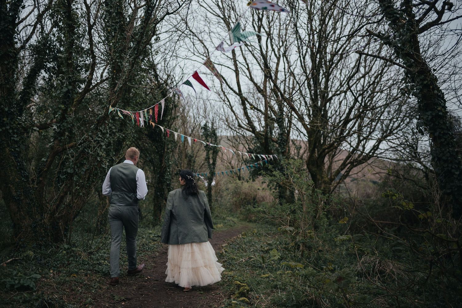 A couple walks through a wooded path decorated with bunting flags overhead.