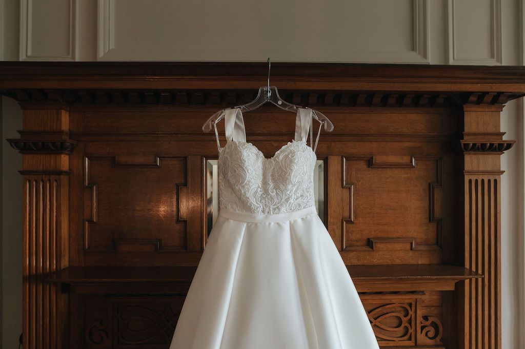 Elegant white wedding dress with lace detailing hanging on wooden wall paneling.