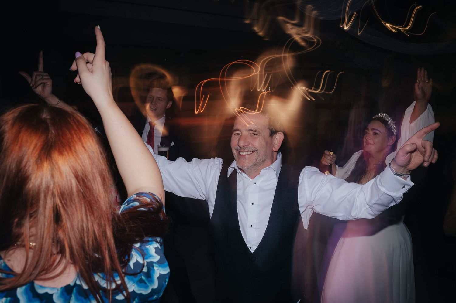 Wedding reception guests dancing together with motion blur and orange light trails in background.