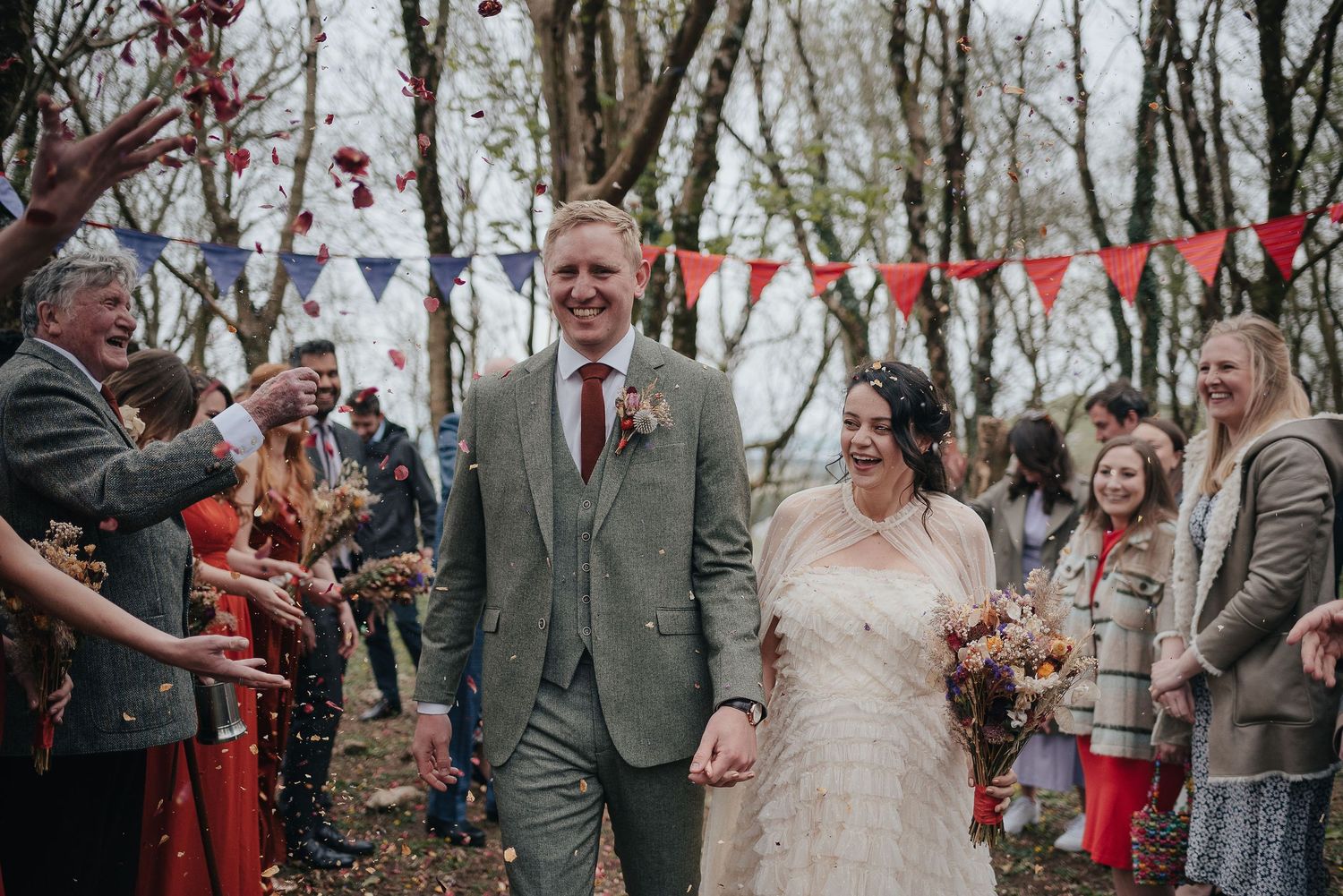 A couple celebrates with guests during their outdoor wedding ceremony with red and white bunting decorations.