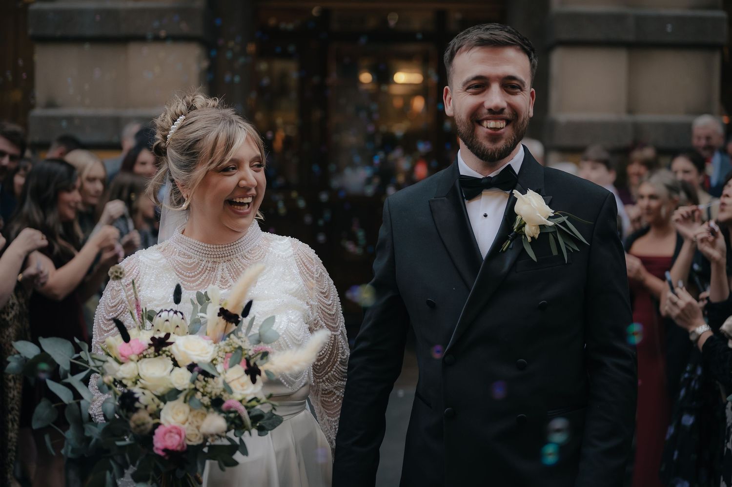 Happy newlyweds share an intimate moment during their outdoor wedding ceremony while guests applaud in background.