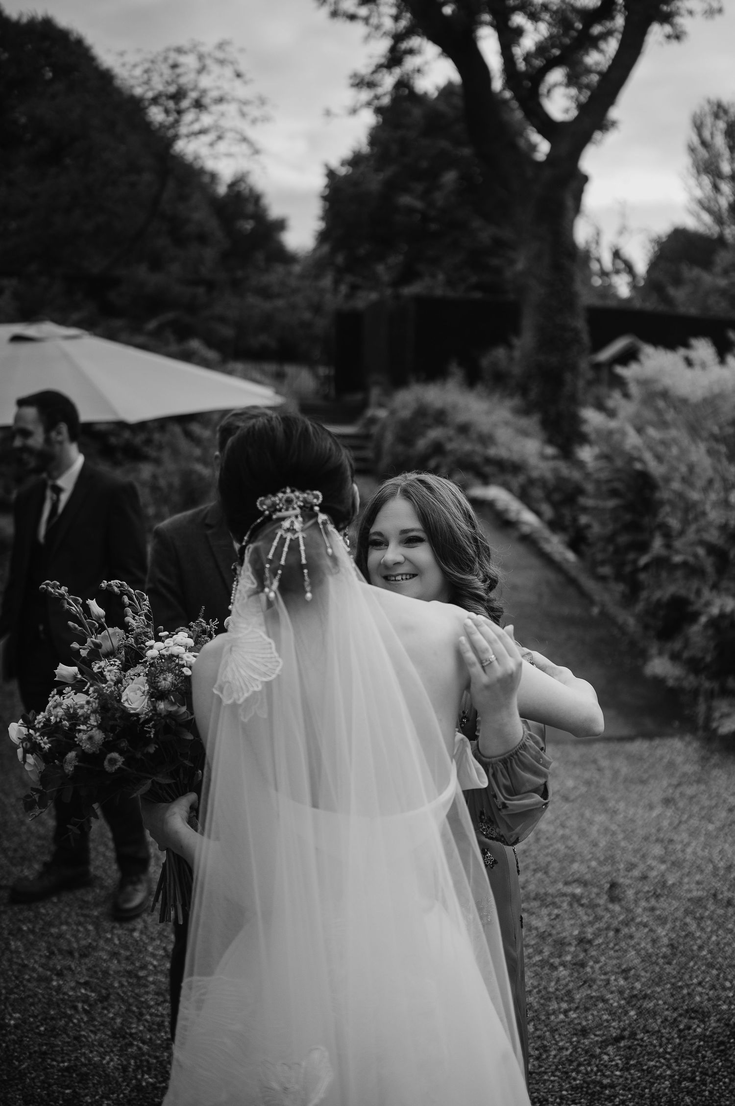 Black and white photo of wedding guests embracing during outdoor garden reception.