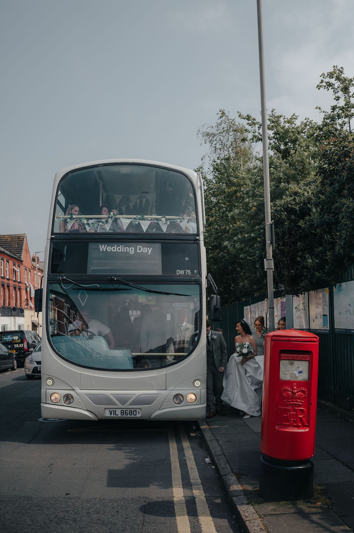 A double-decker wedding bus parked next to a red British post box on a city street.
