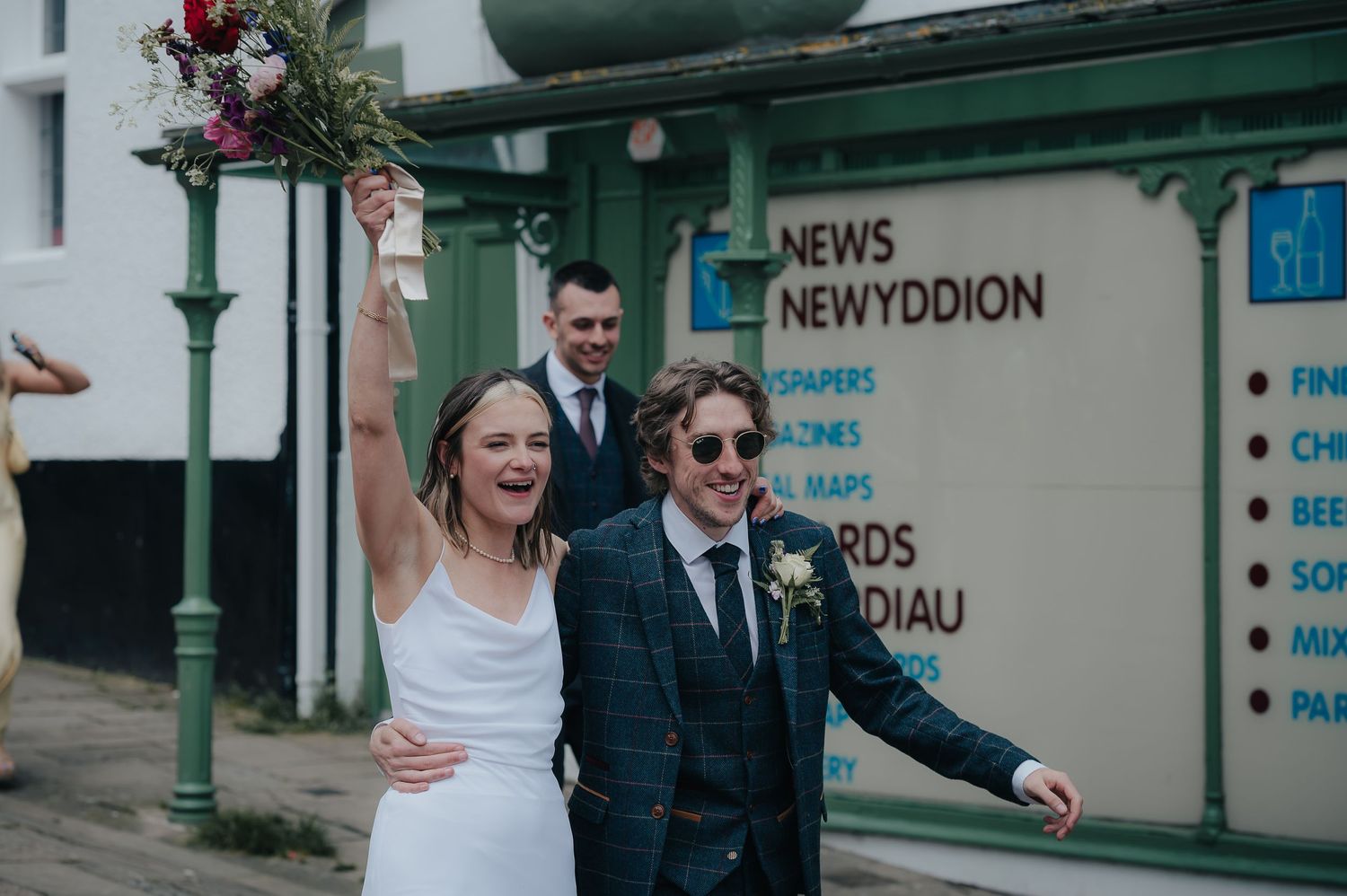 Cheerful couple celebrating outside a storefront on their wedding day.