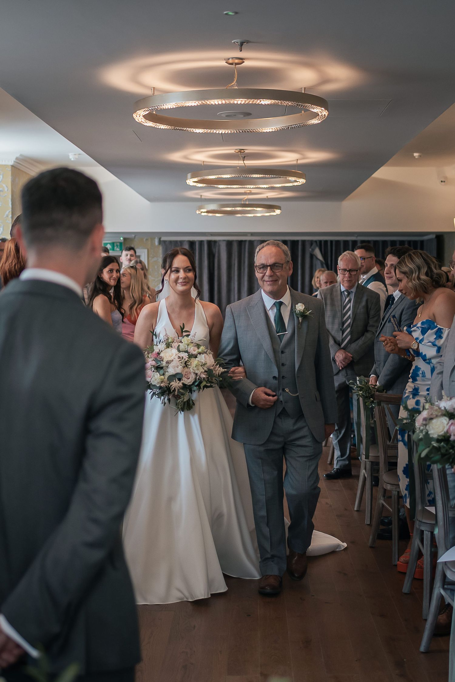 Wedding ceremony under modern circular chandeliers in an elegant indoor venue.