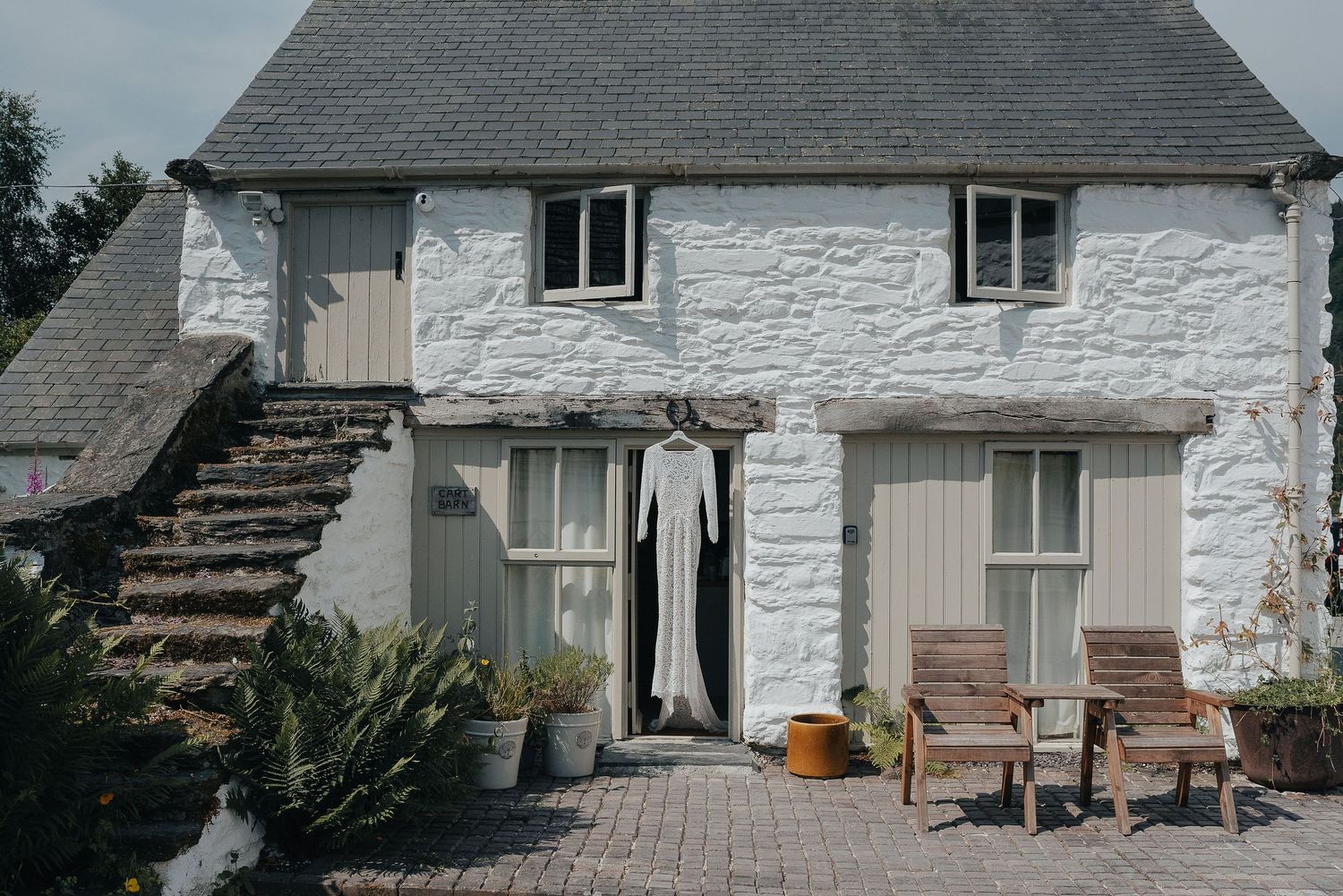 Rustic white cottage with grey roof and a wedding dress hanging outside.