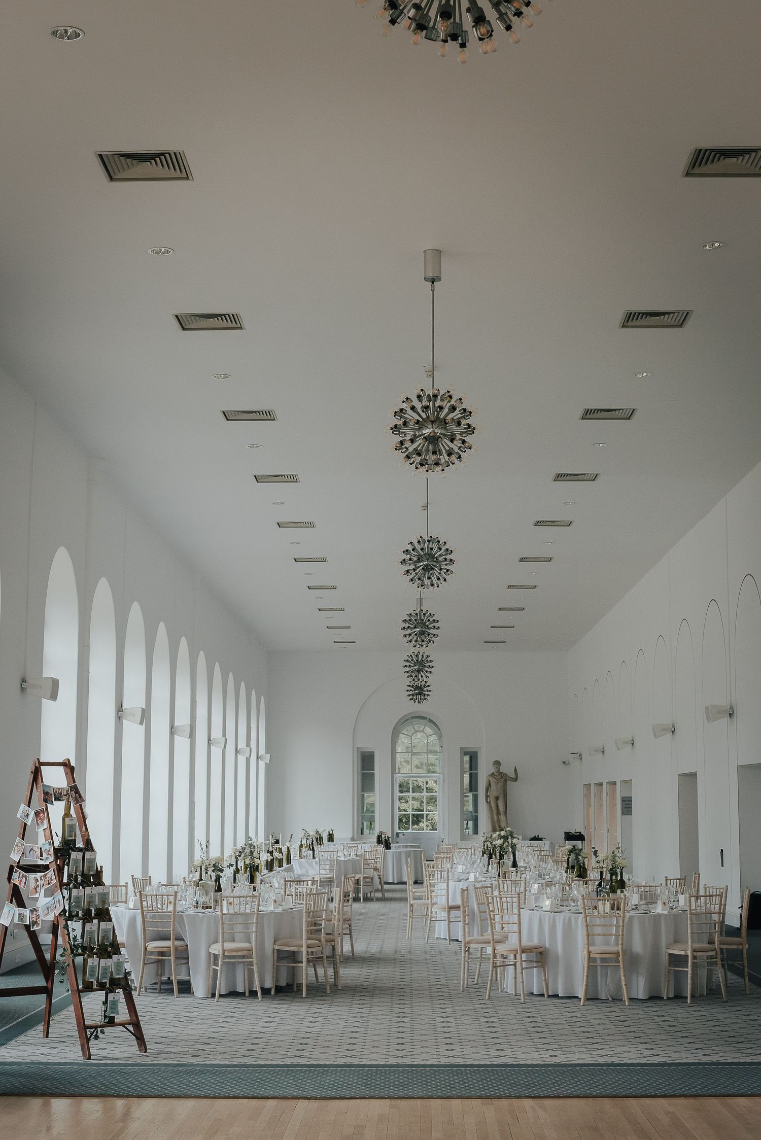 Elegant white wedding reception hall with arched windows and modern sputnik chandeliers.