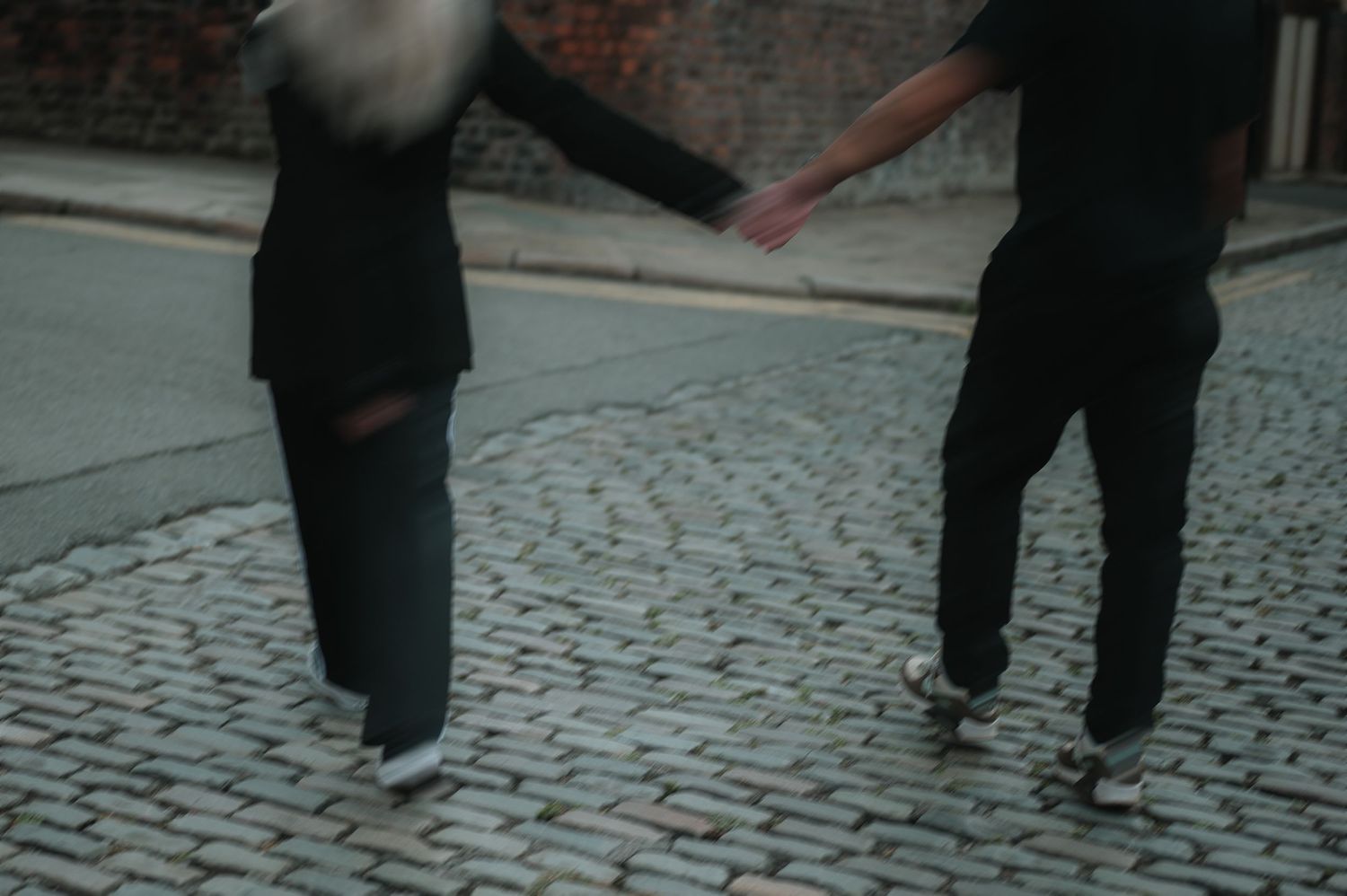 Two people holding hands while walking on a cobblestone street, captured in a blurry, artistic style.