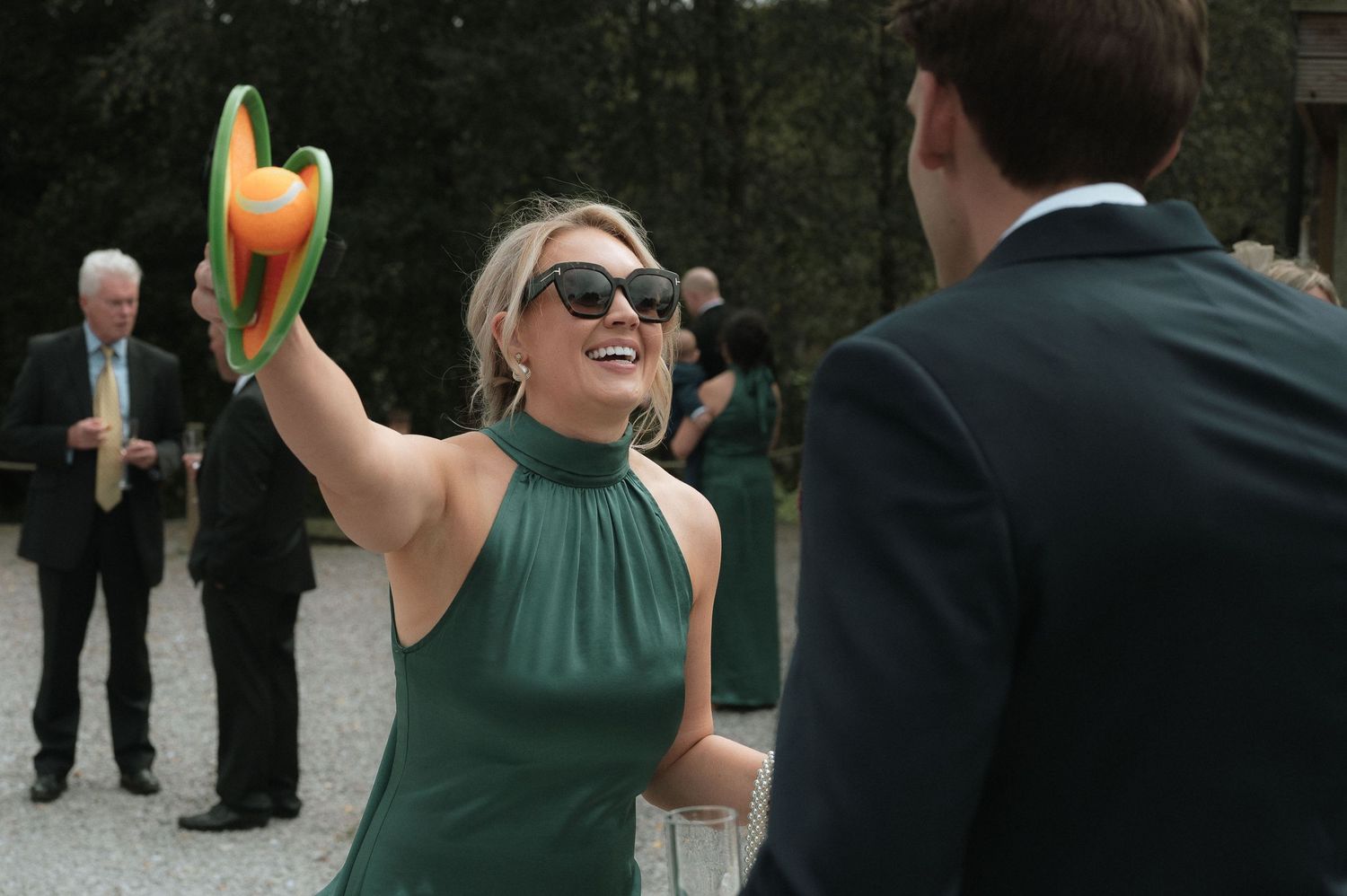 A group of people in dark coats and green shirts reach up to catch oranges being tossed at an outdoor event.