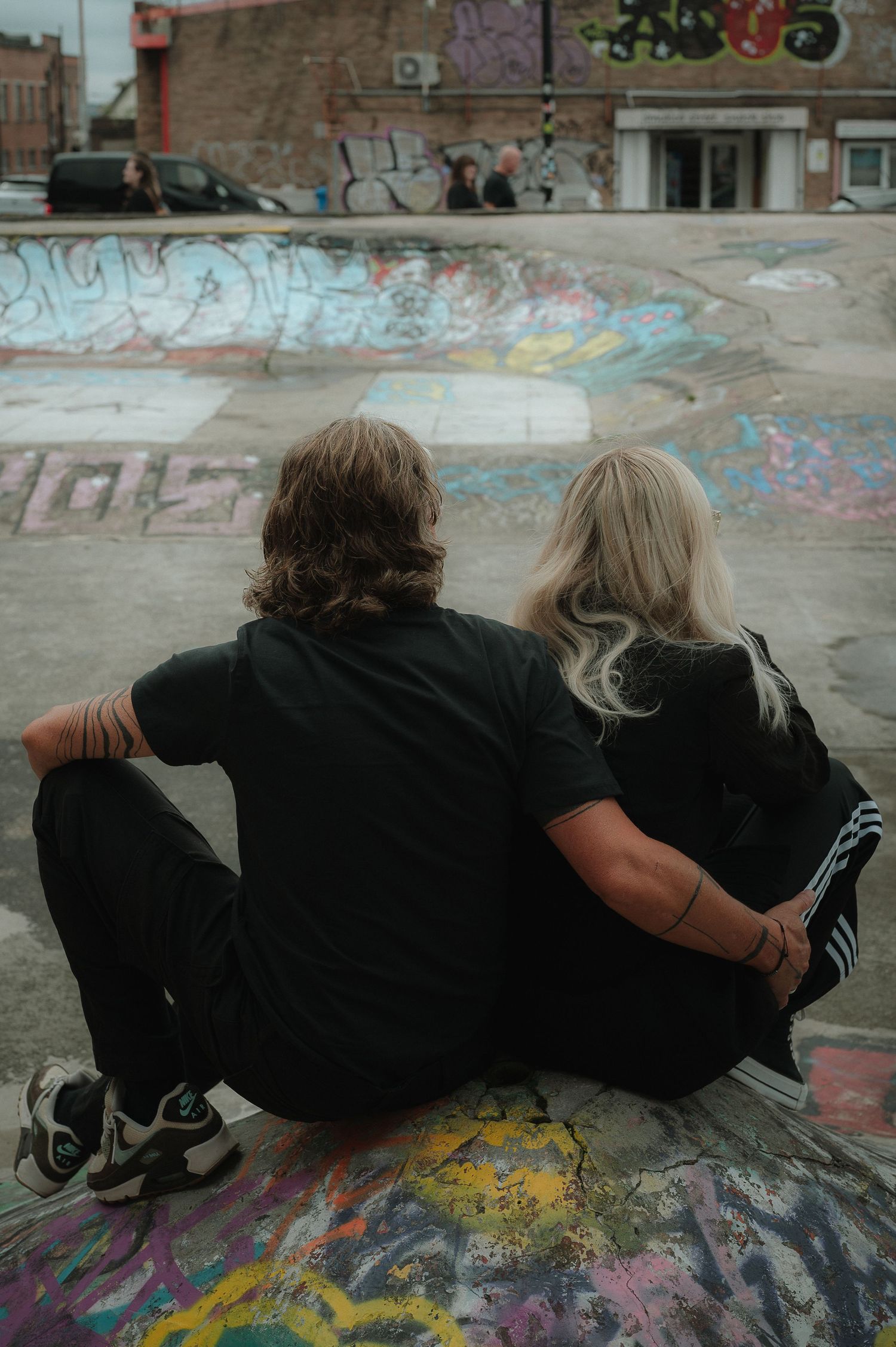 Two people in black clothing lie side by side on a colorful graffiti-covered surface.