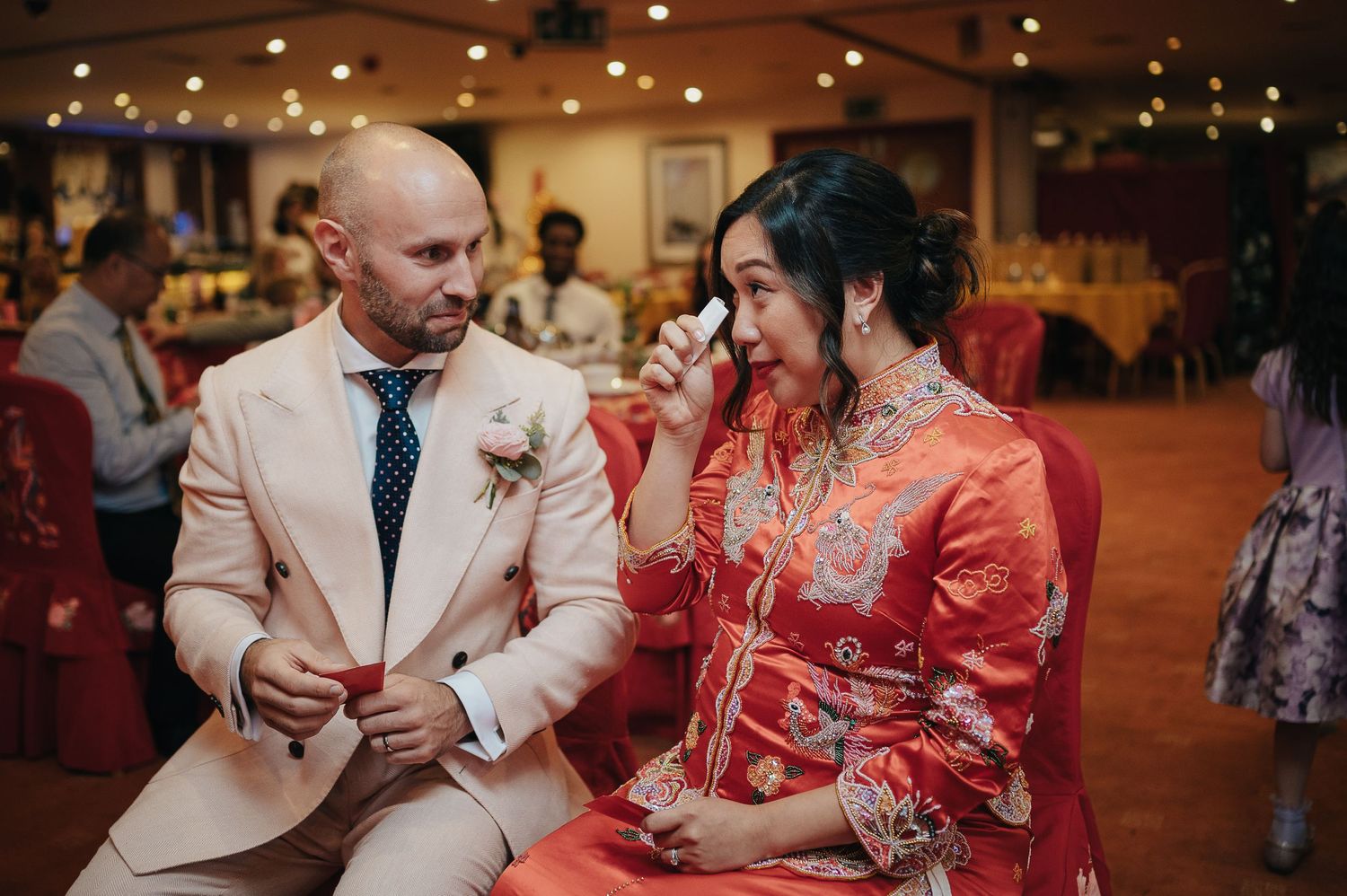A wedding couple celebrates at their reception in formal western and traditional red attire.