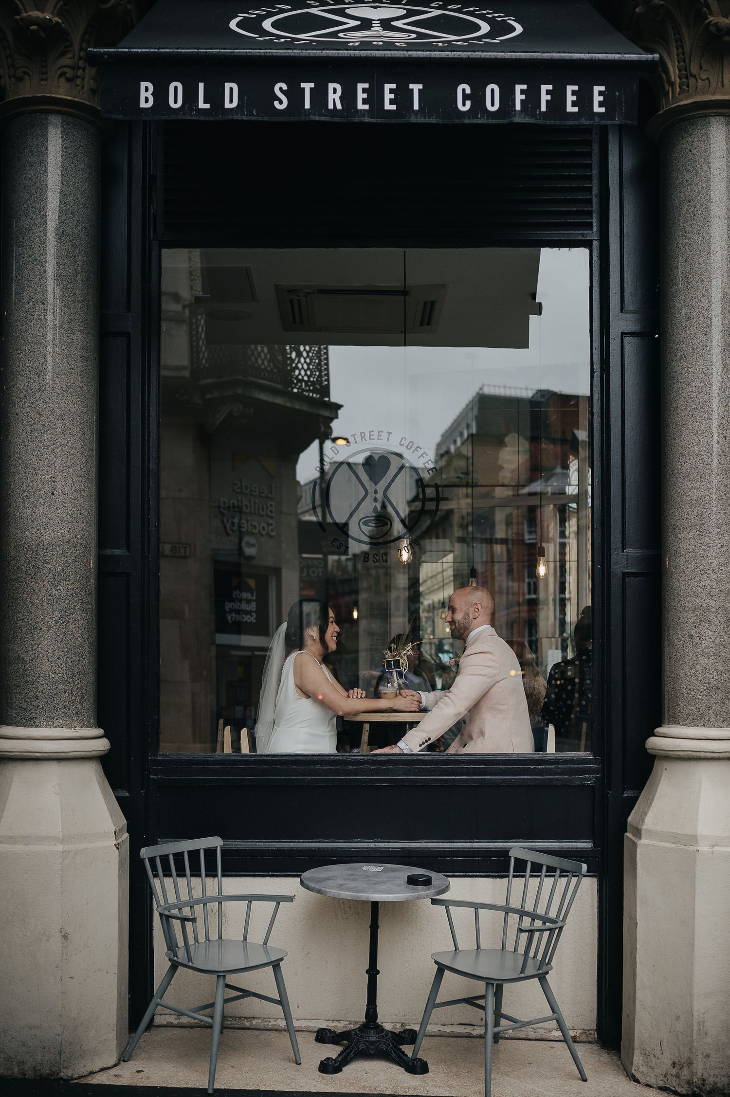View through Bold Street Coffee shop window showing couple seated at a small cafe table.