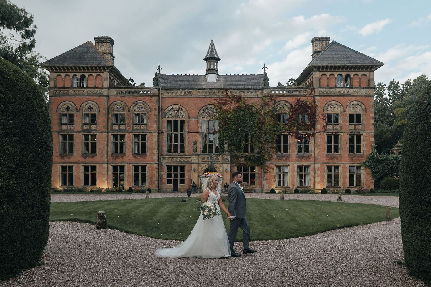 Stunning red brick Victorian mansion serves as backdrop for wedding photography on manicured grounds.