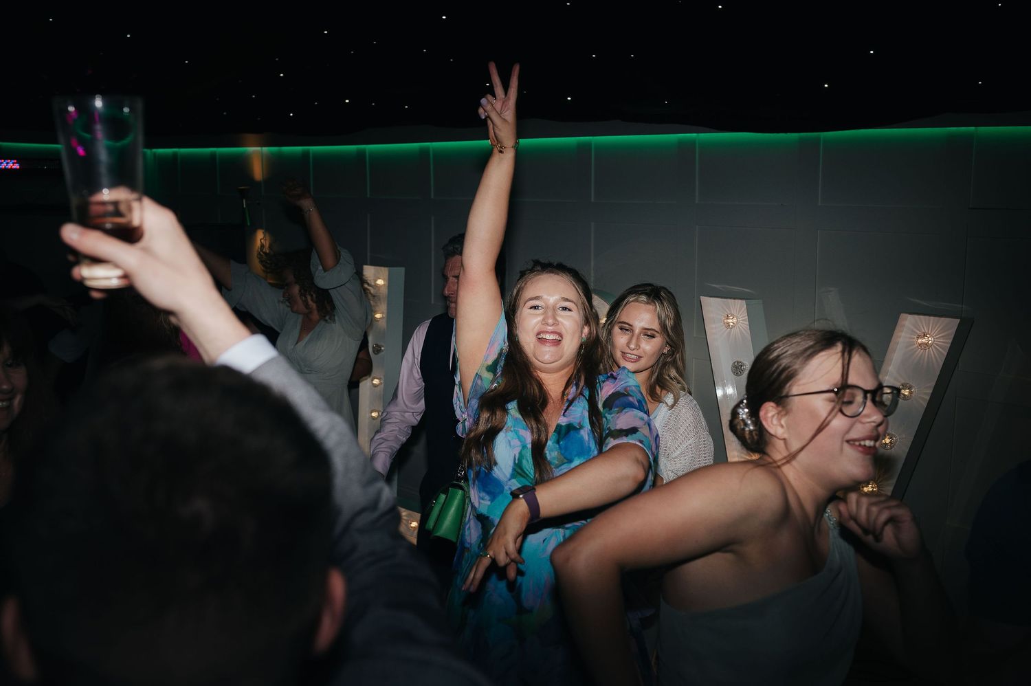 Wedding reception guests dancing and celebrating under neon lights at a nighttime party.