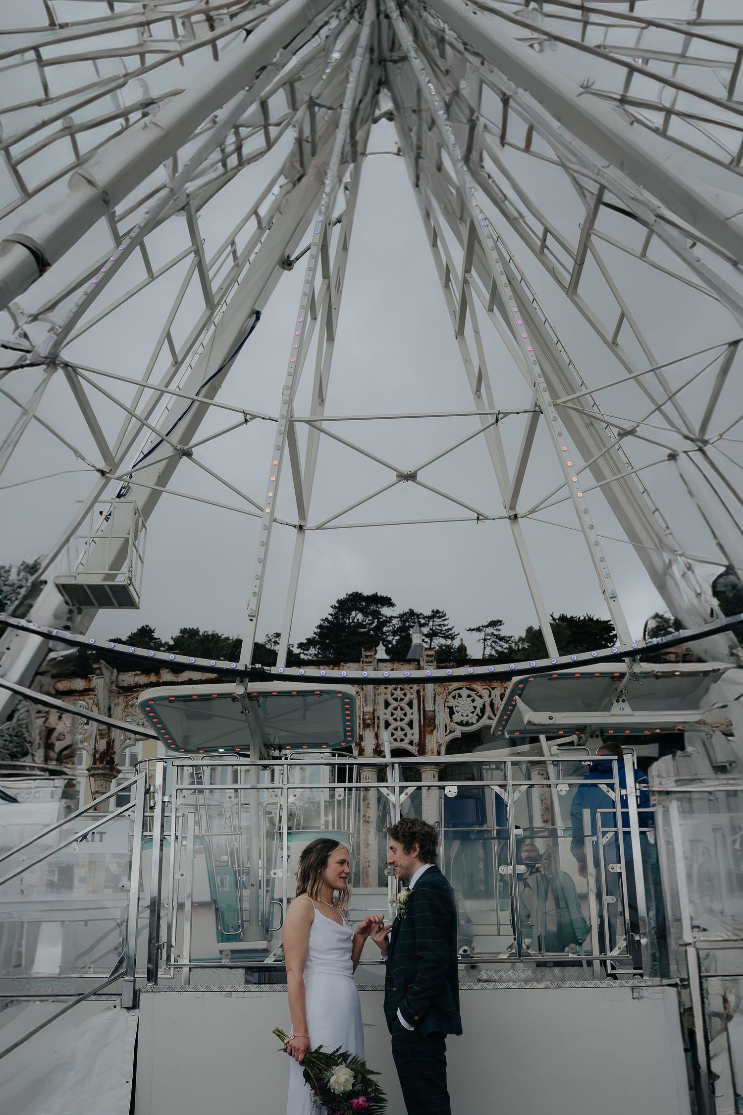 Couple standing under geometric white metal structure of a ferris wheel or observation point.