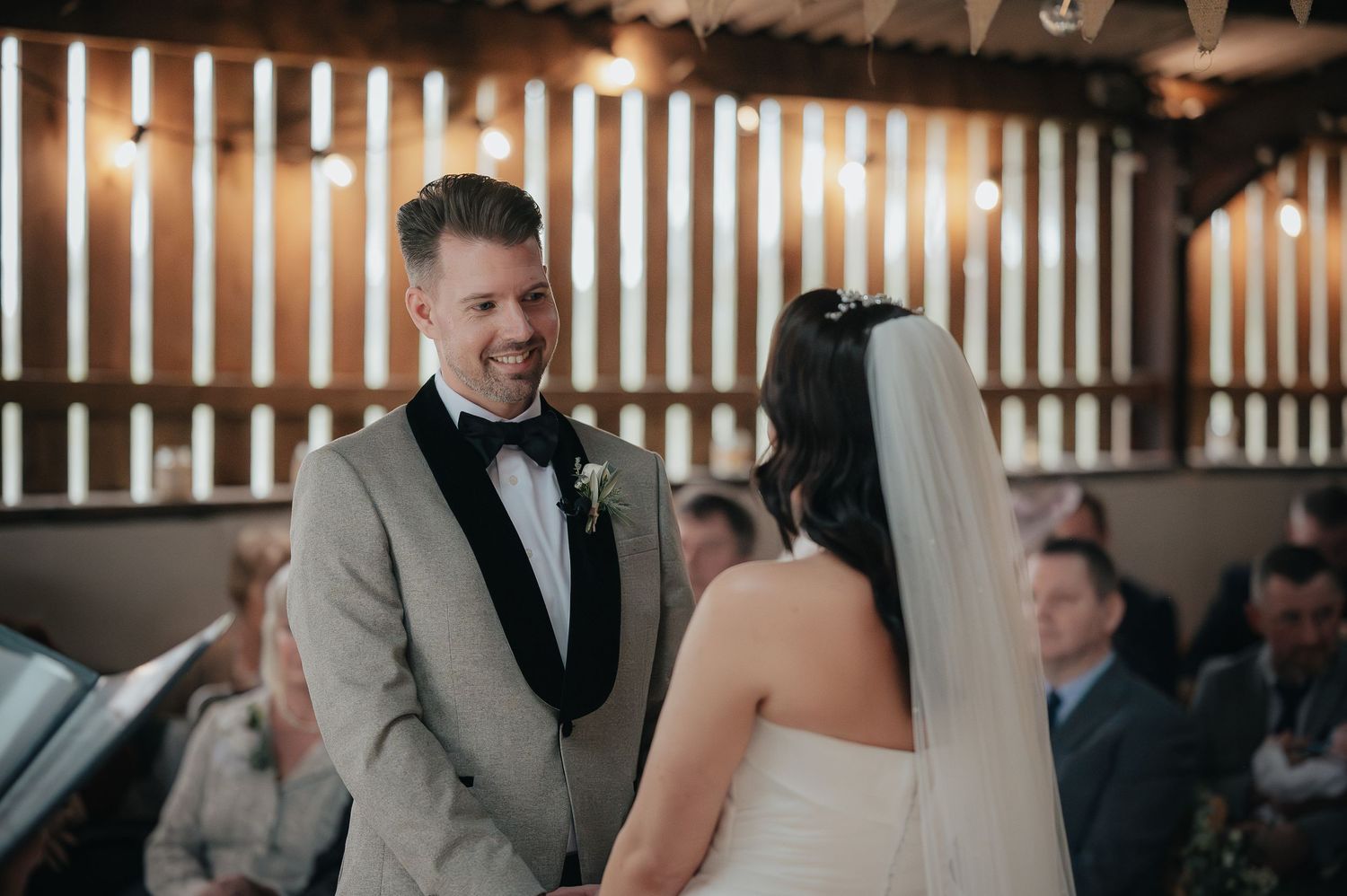 A couple exchanges vows during an intimate indoor wedding ceremony with rustic wooden decor.