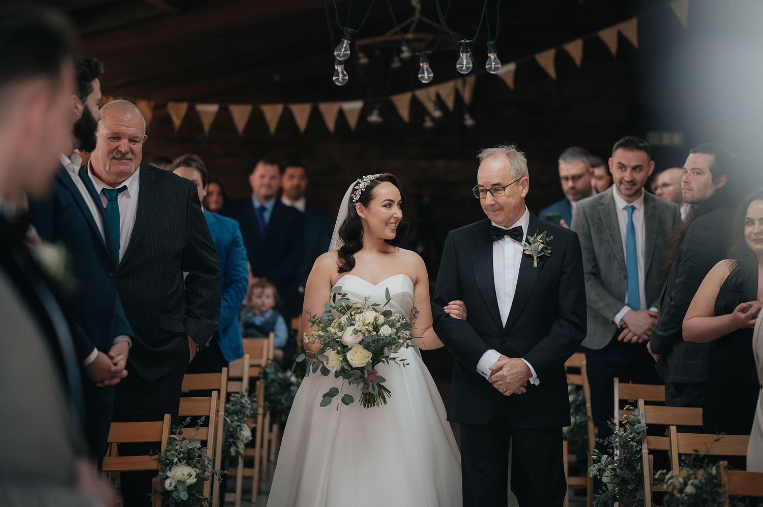 Wedding ceremony in rustic venue with string lights and orange bunting decorations overhead.