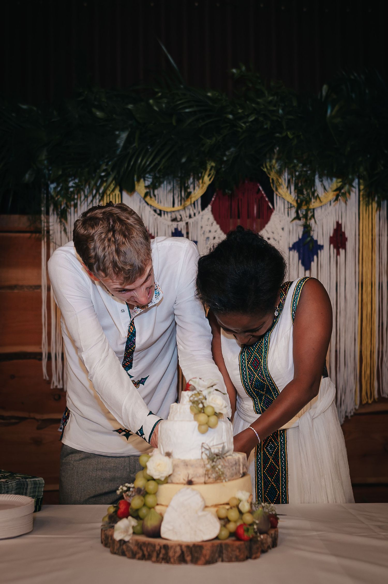 Couple cutting their wedding cake together on wooden stand with floral backdrop.