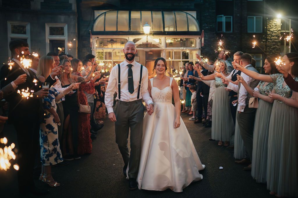 Sparkler exit with wedding couple walking through tunnel of guests holding lit sparklers at night.
