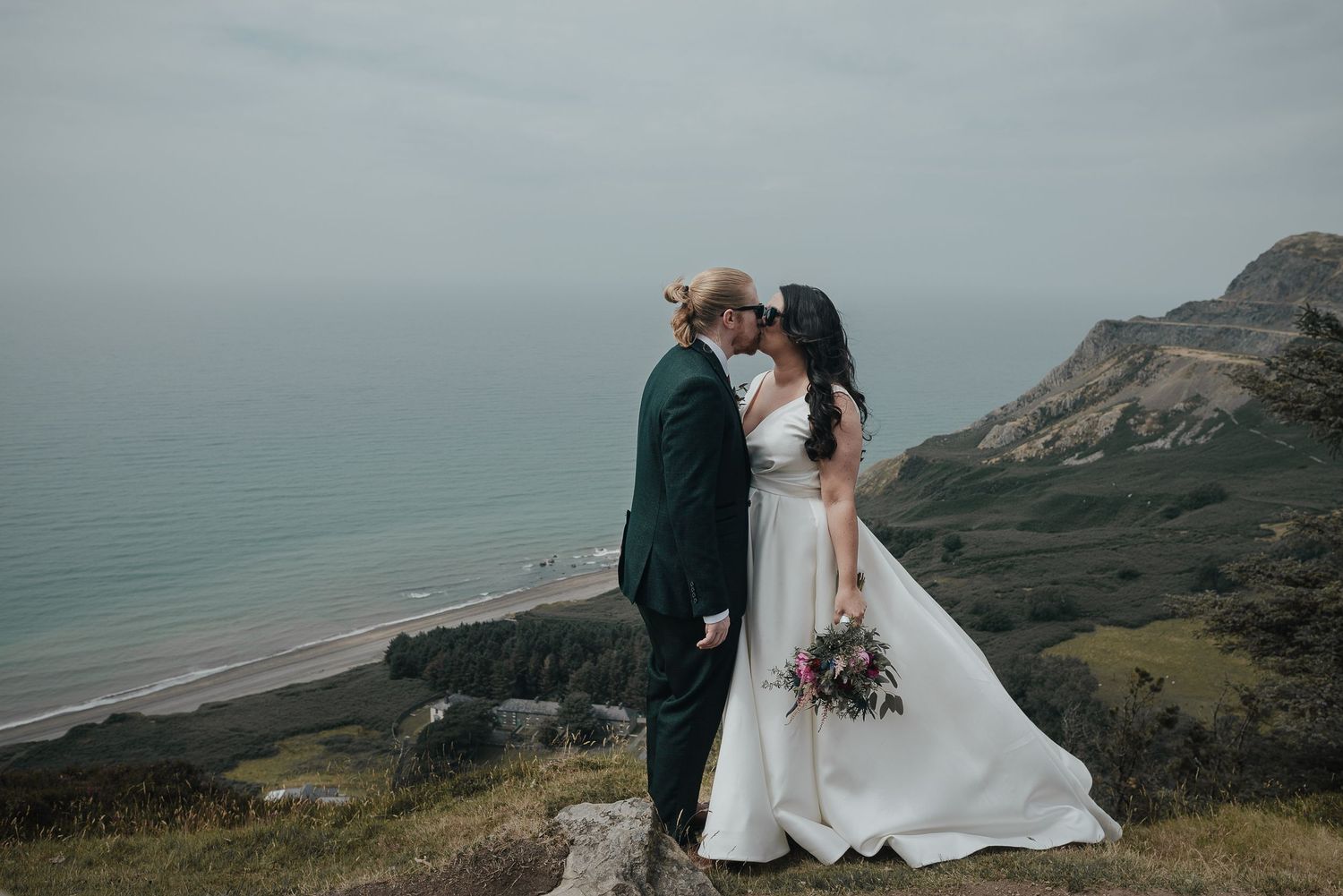 A couple shares an intimate moment on a clifftop overlooking a dramatic coastal landscape.