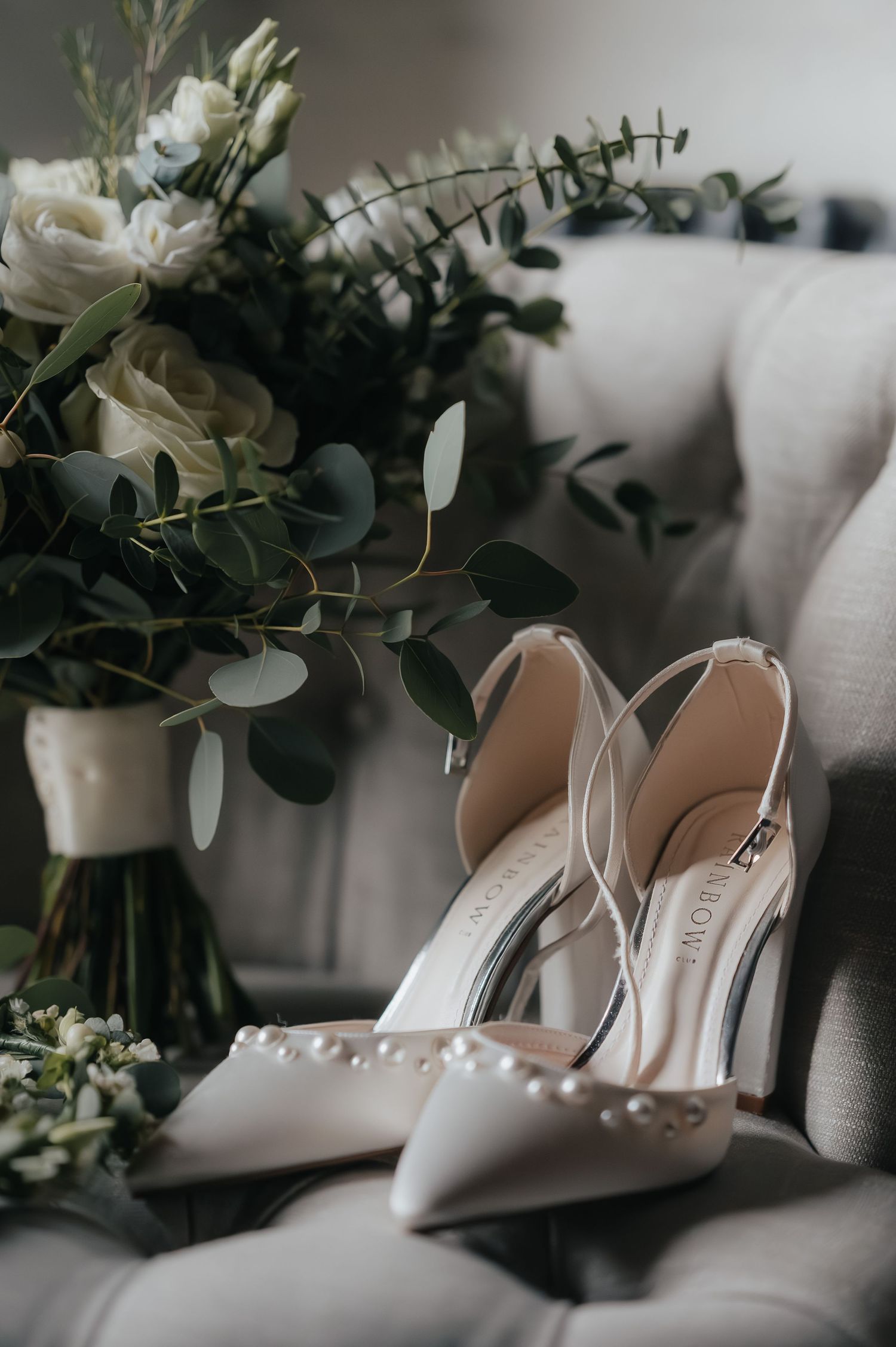 White bridal shoes next to elegant floral arrangement with roses and eucalyptus.