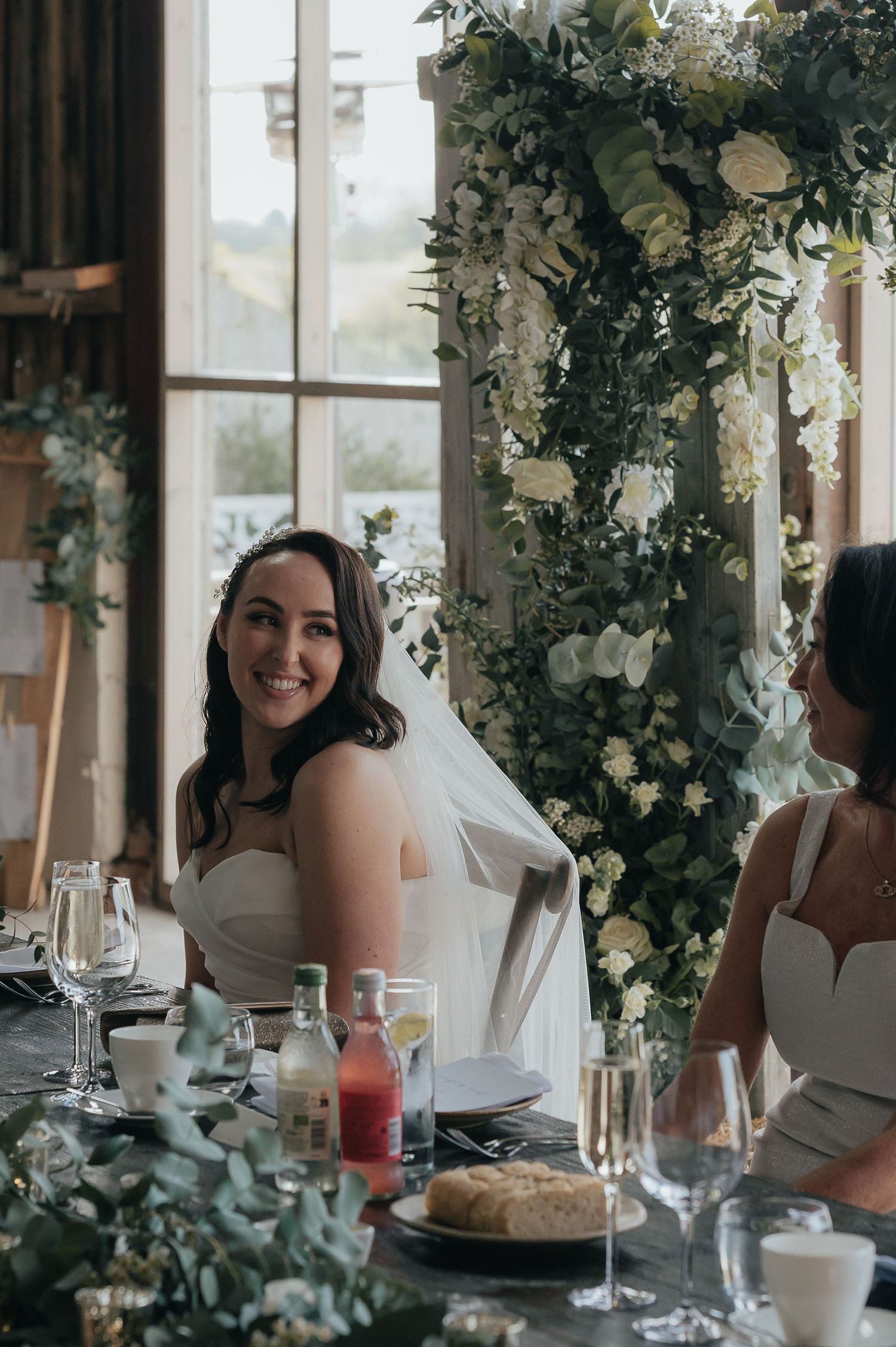 Bride seated at decorated reception table with elegant floral arrangements and place settings.