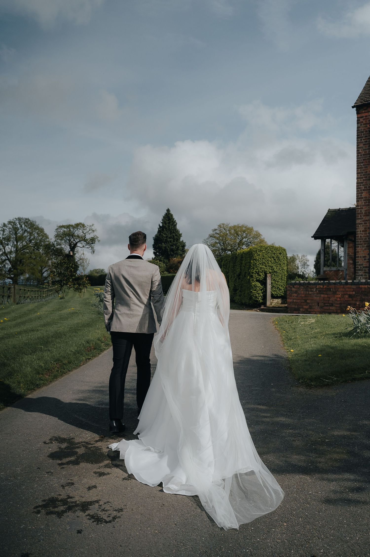 Couple in wedding attire walking along a scenic garden path on their special day.