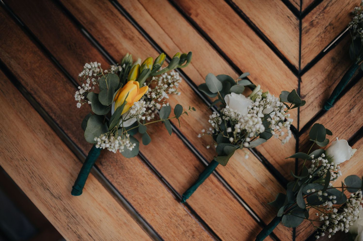 Wedding boutonnieres with yellow tulips and baby's breath on wooden surface.