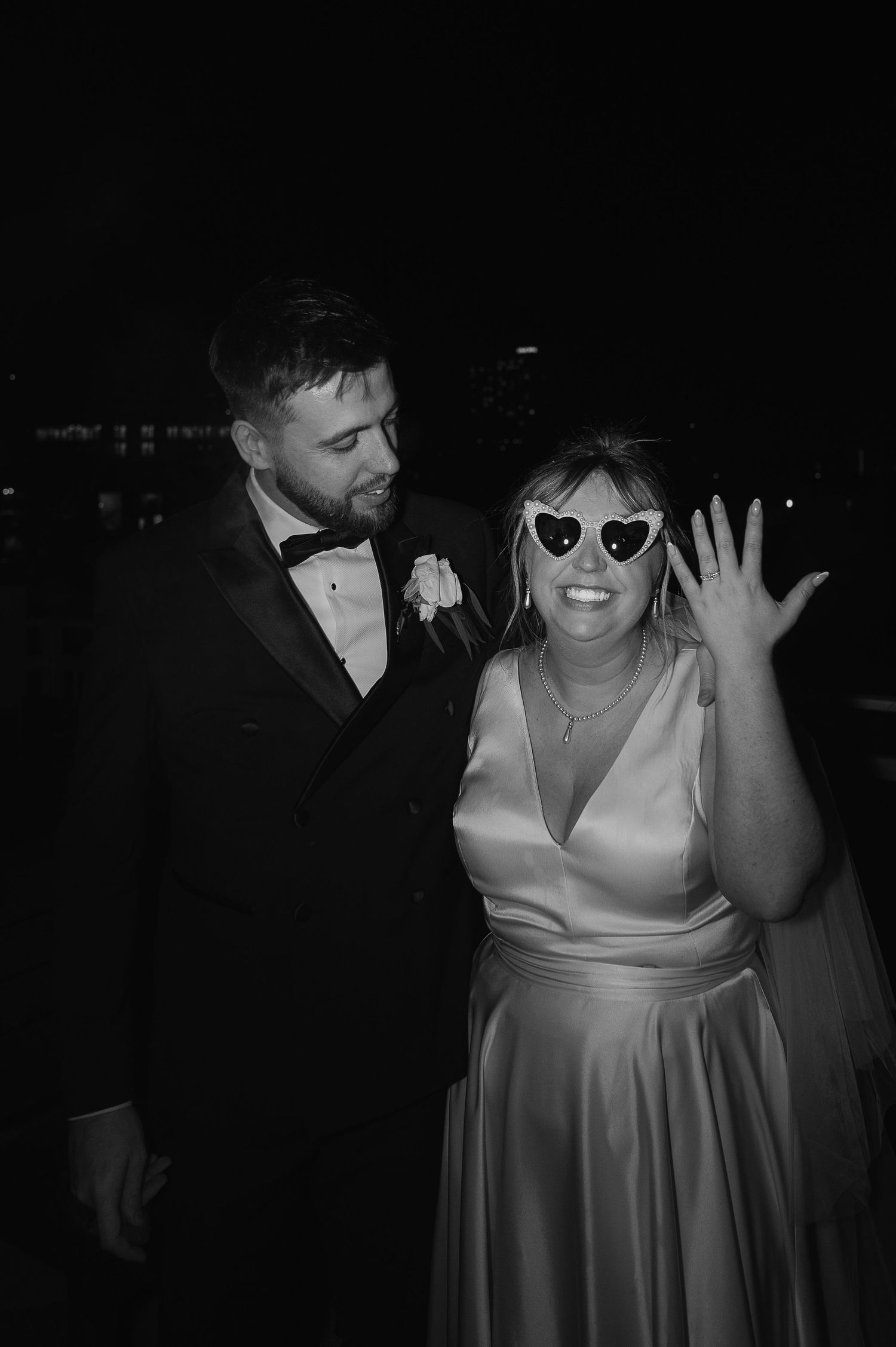 A joyful black and white wedding photo with the bride wearing heart-shaped sunglasses and a satin dress.