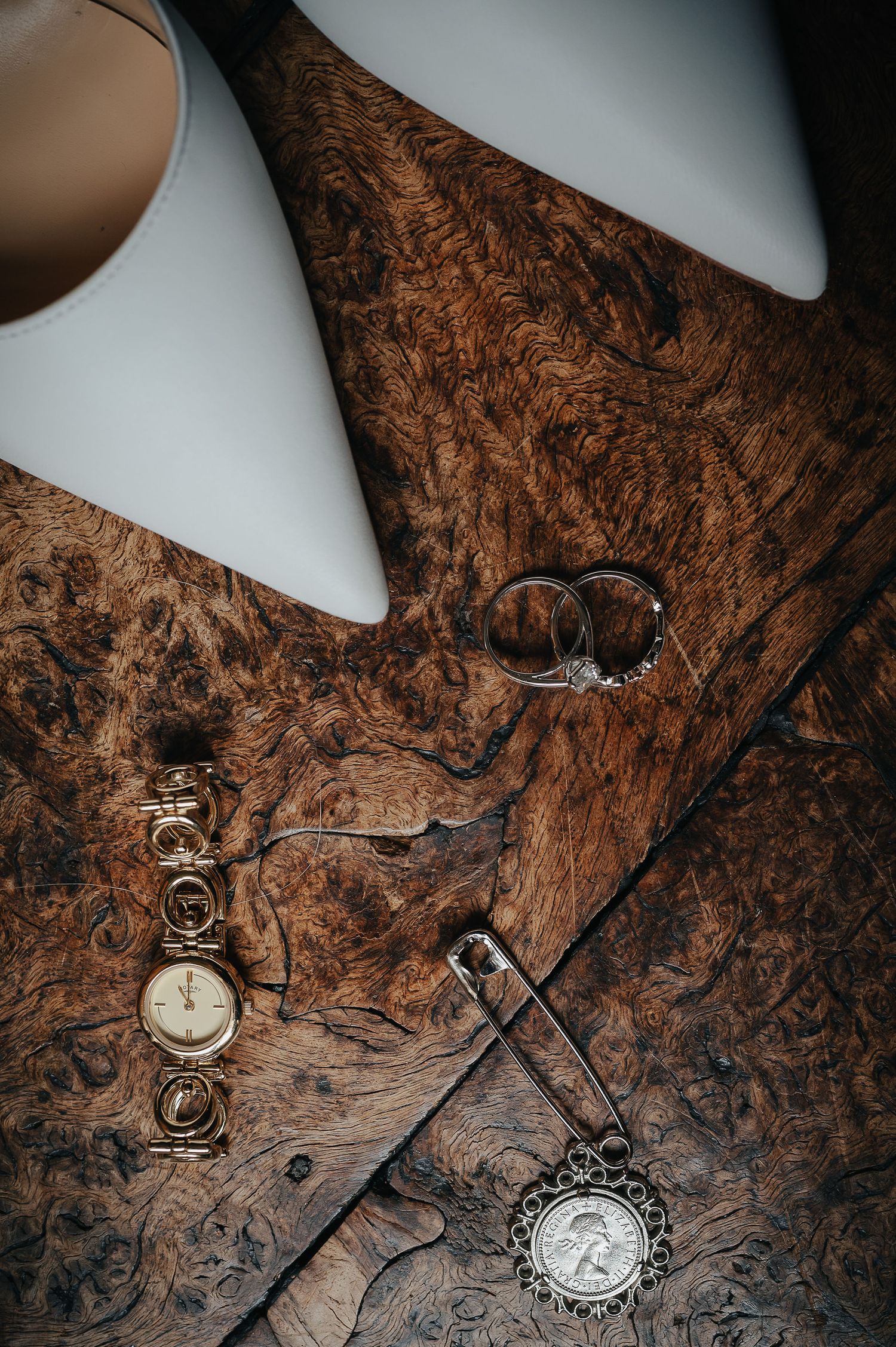Wedding accessories including rings, watches, and white shoes arranged on textured wooden surface.