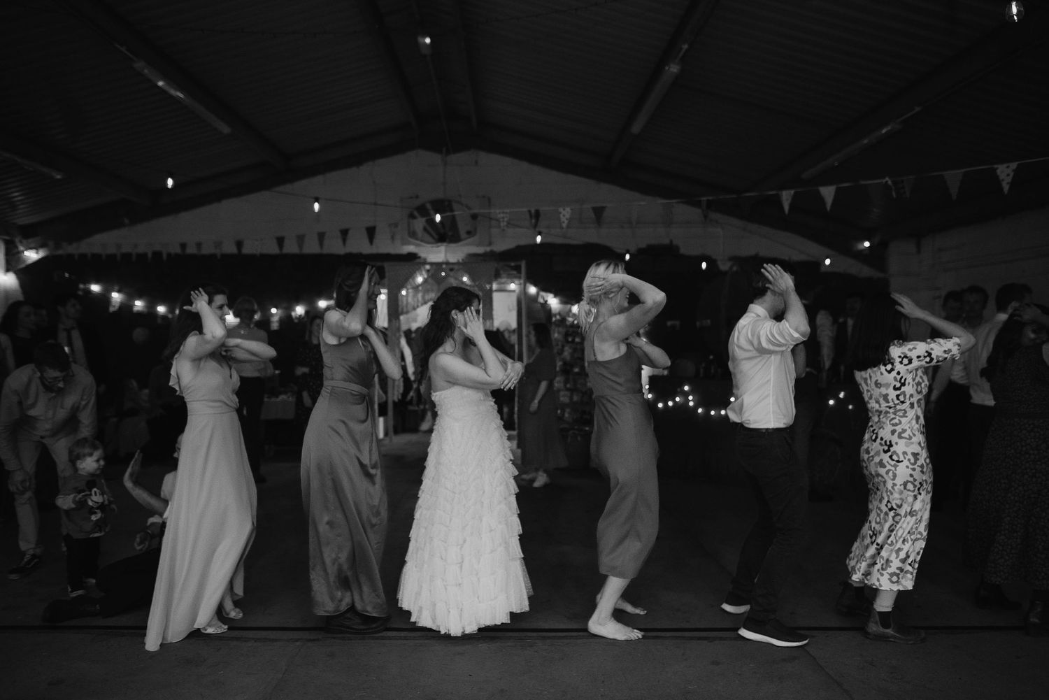 Black and white photo of wedding guests dancing in formation at an evening reception.