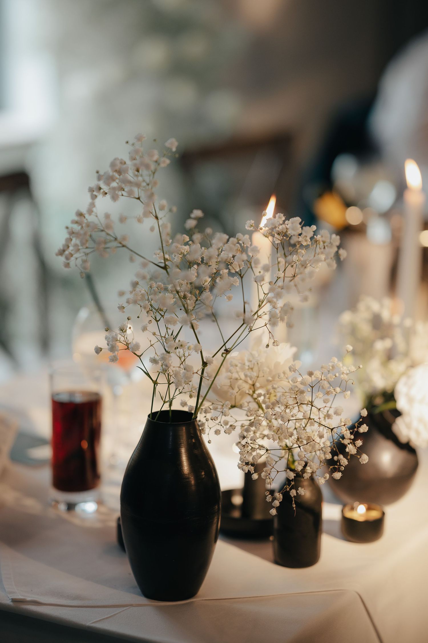 Delicate baby's breath flowers arranged in black vases with candlelight on a white tablecloth.