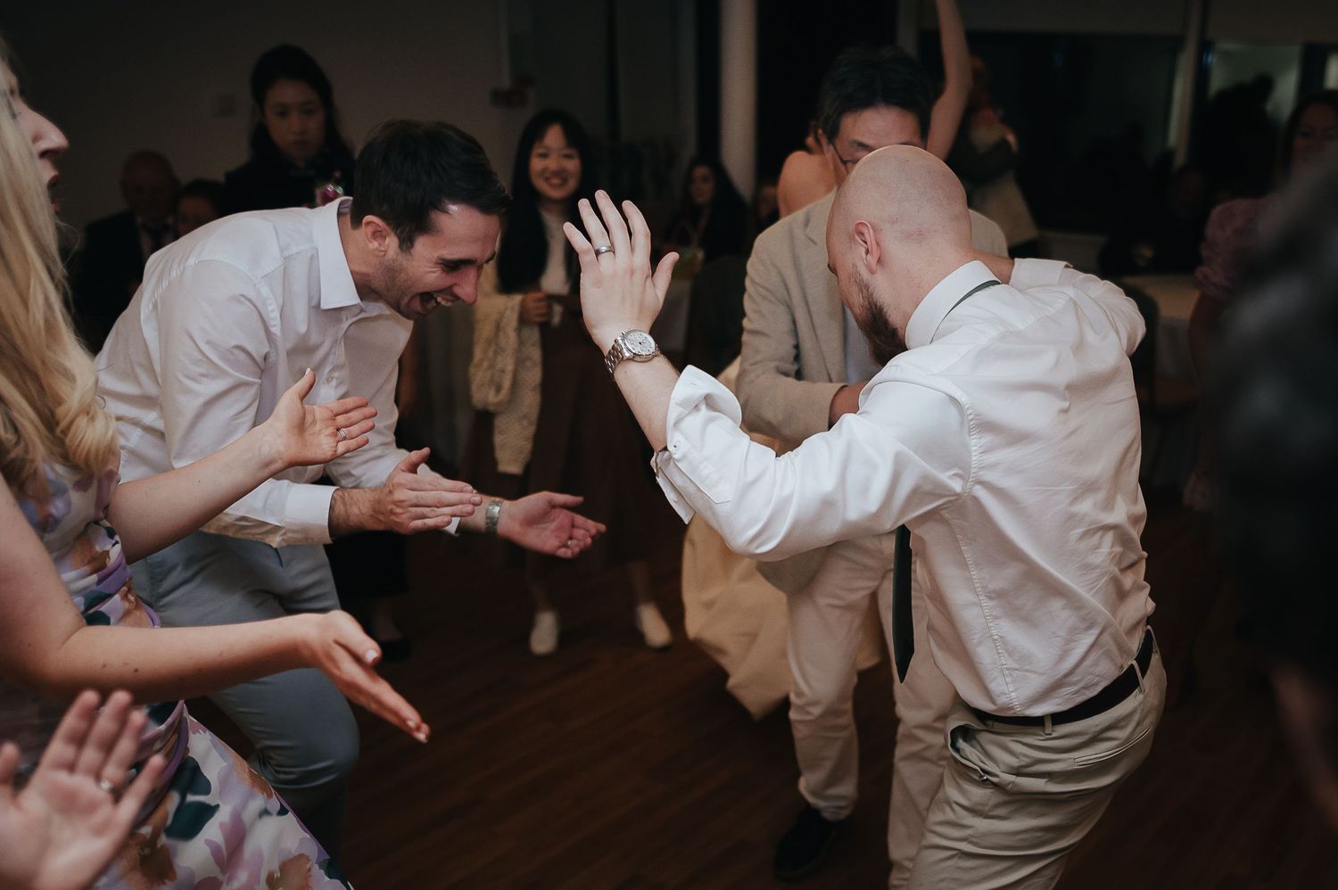 Wedding guests dance enthusiastically on a dark wooden dance floor.
