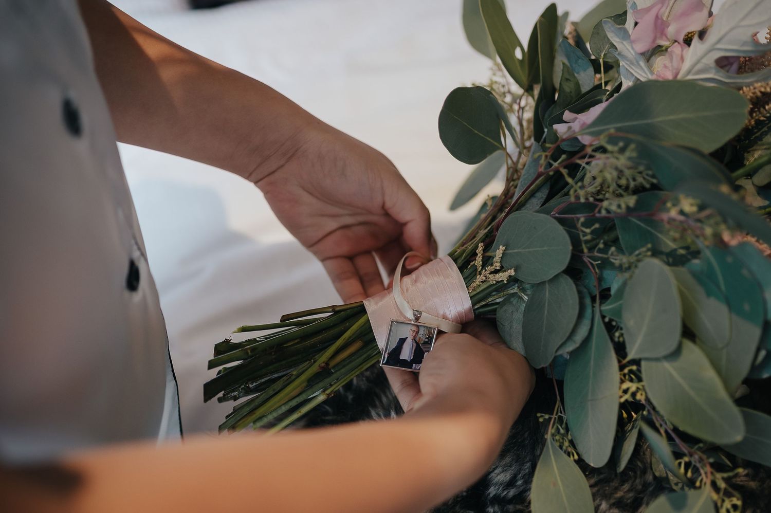 Hands adjusting a wedding bouquet with eucalyptus leaves and flowers.