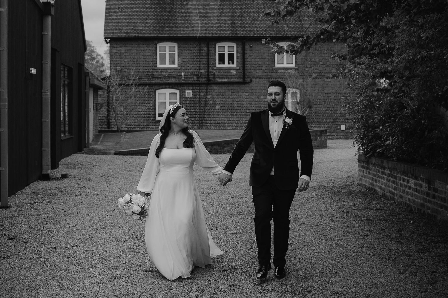 A couple walking together outside a rustic brick building on their wedding day.
