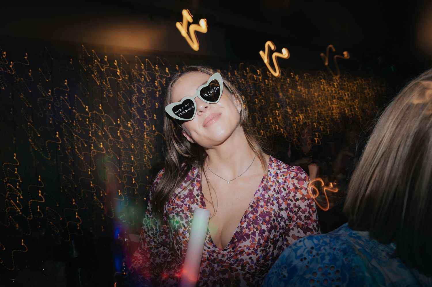 Party guest in sunglasses and floral dress poses during a celebration.