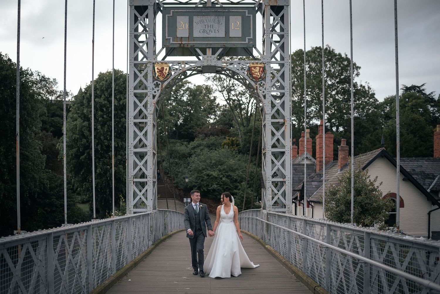 Couple walking across vintage metal bridge in wedding attire.