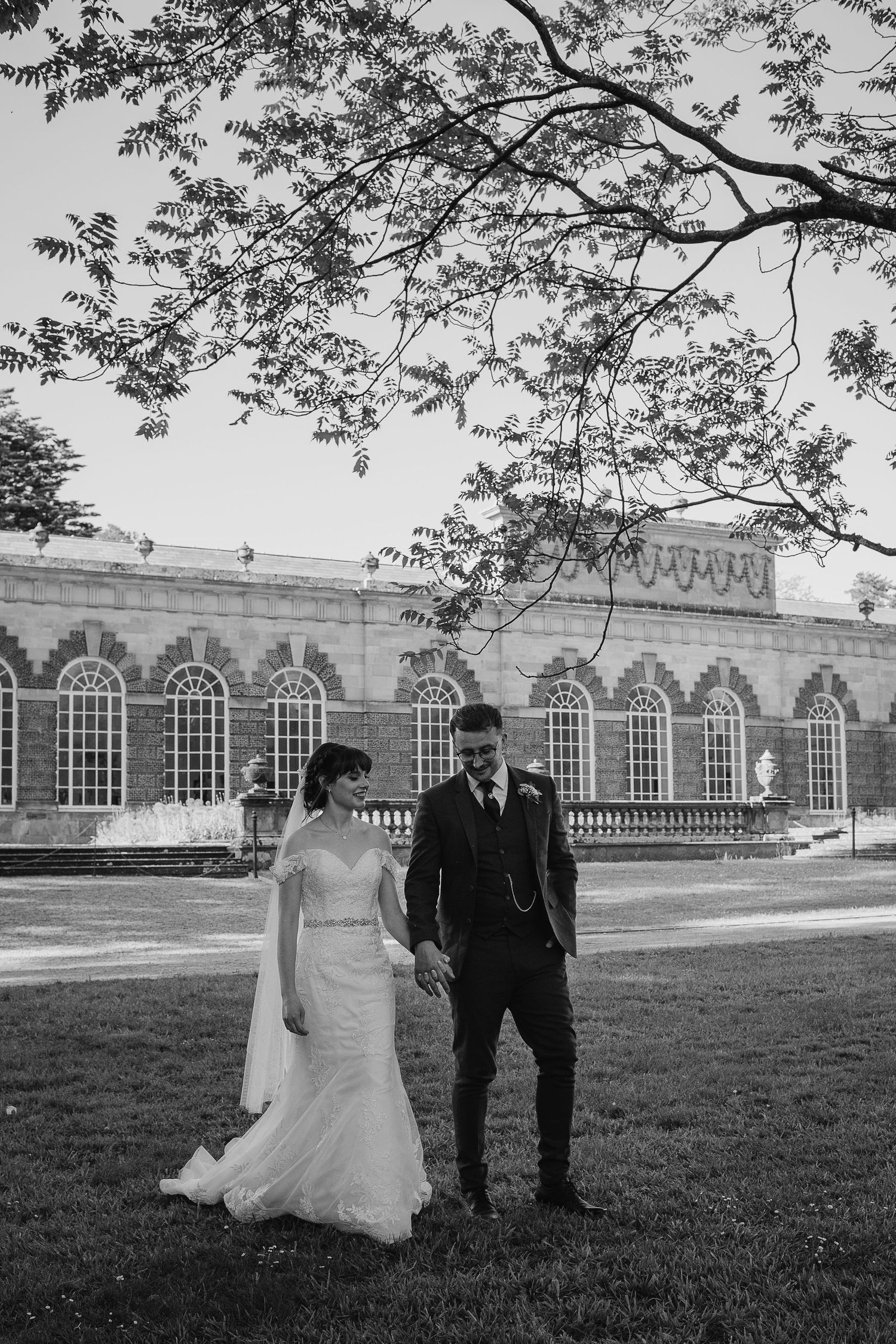 Black and white wedding photo in front of a historic building with arched windows.