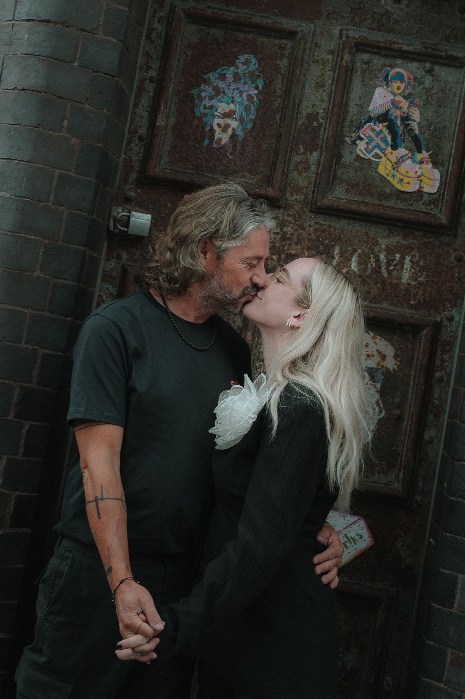 A series of four black and white photos showing a couple in an intimate moment against a dark brick wall.