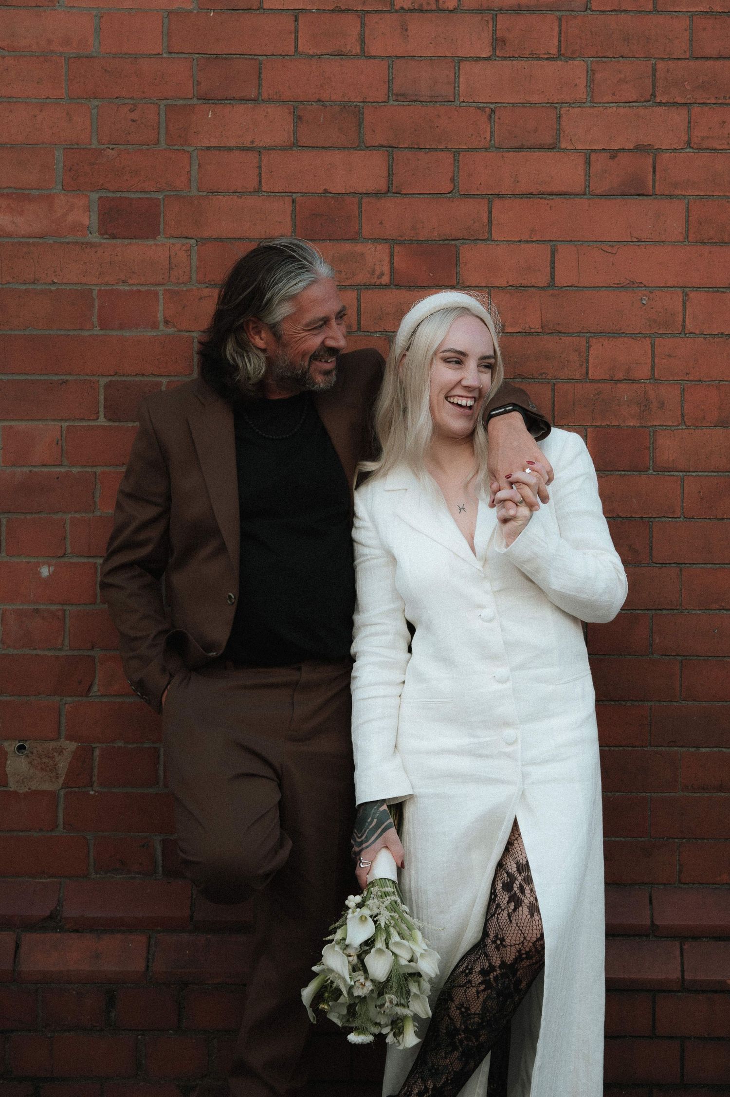 Couple sharing an intimate moment against a rustic red brick wall.