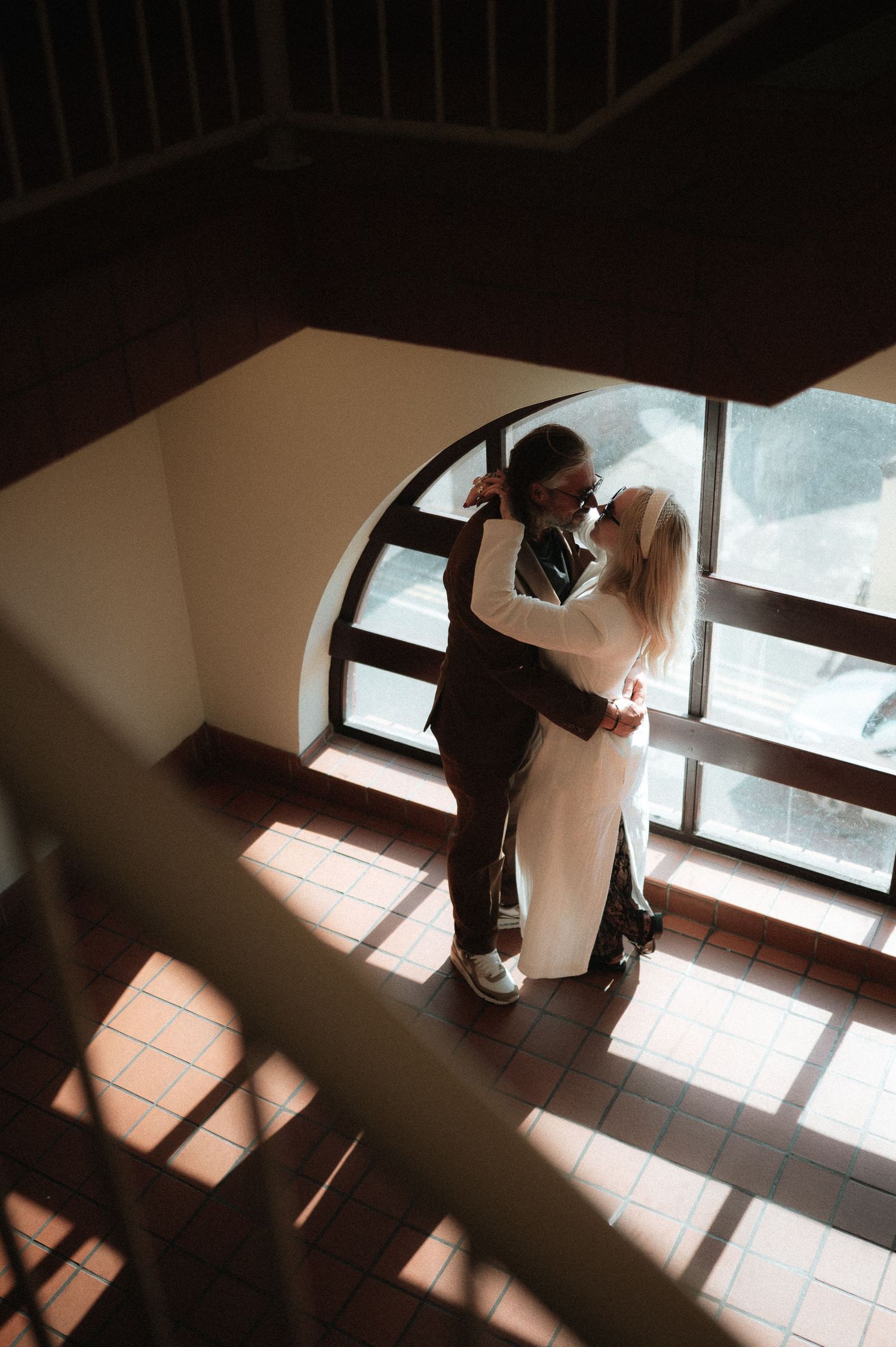 Two people standing in dramatic window light casting shadows on tiled floor.
