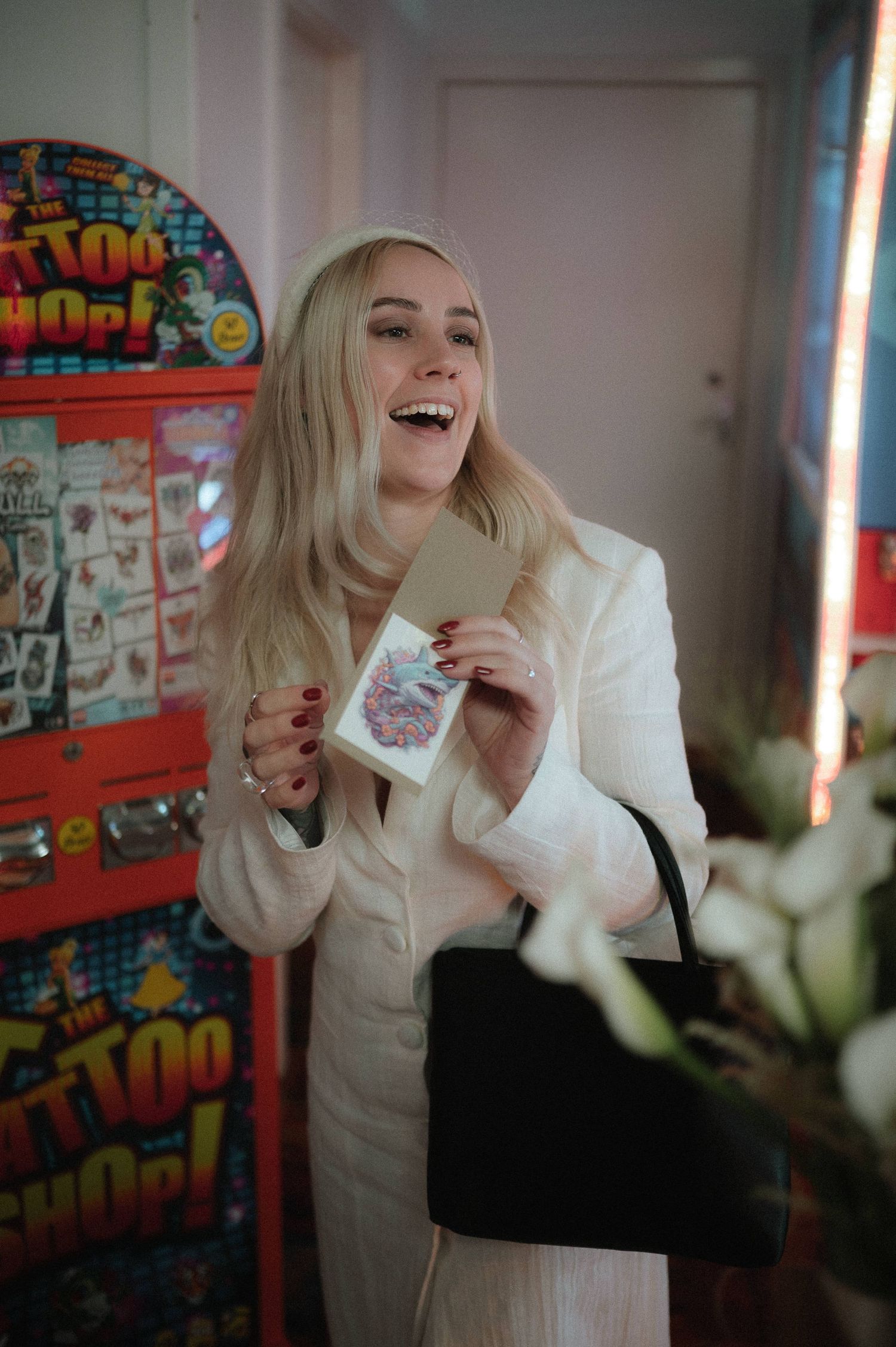 A person in a white blazer enjoys a beverage in an indoor setting with colorful wall art in the background.