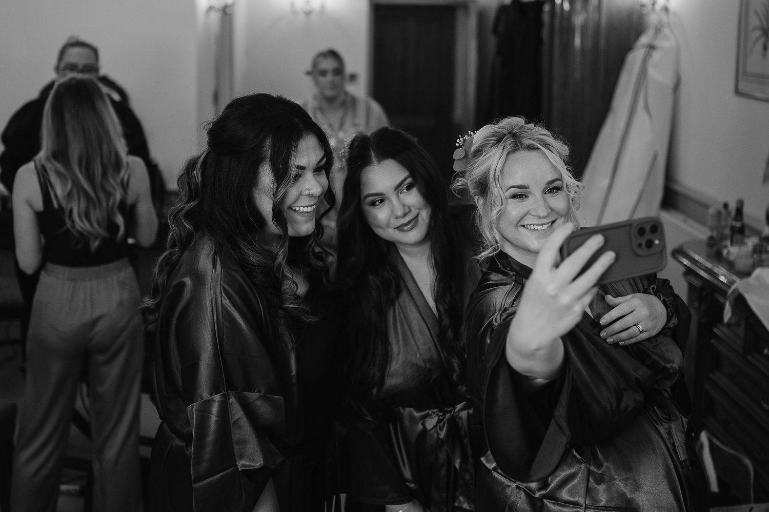 Friends in dark robes take a celebratory selfie during wedding preparations.