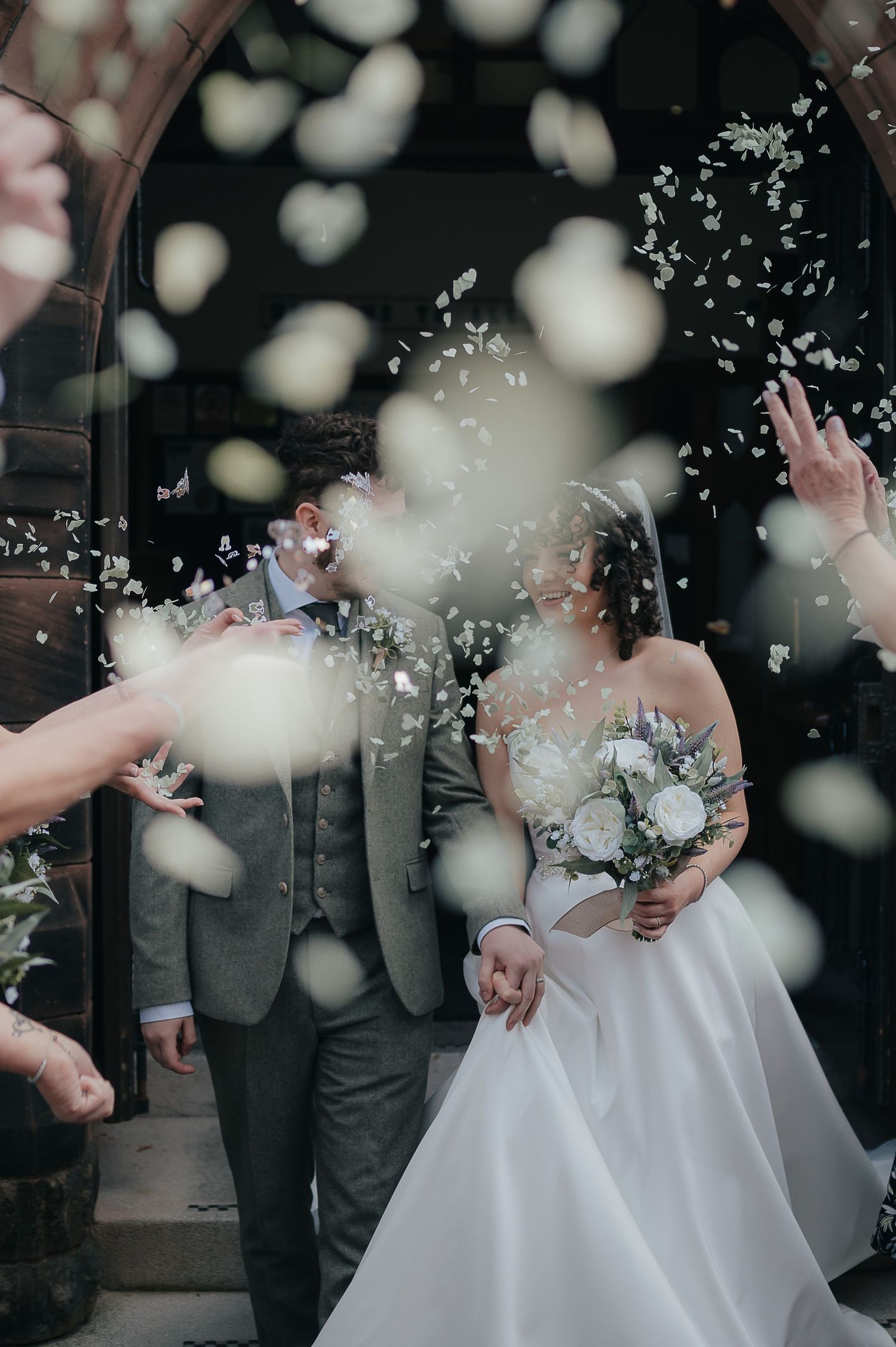 Confetti and flower petals being thrown over a wedding couple outside a church entrance.