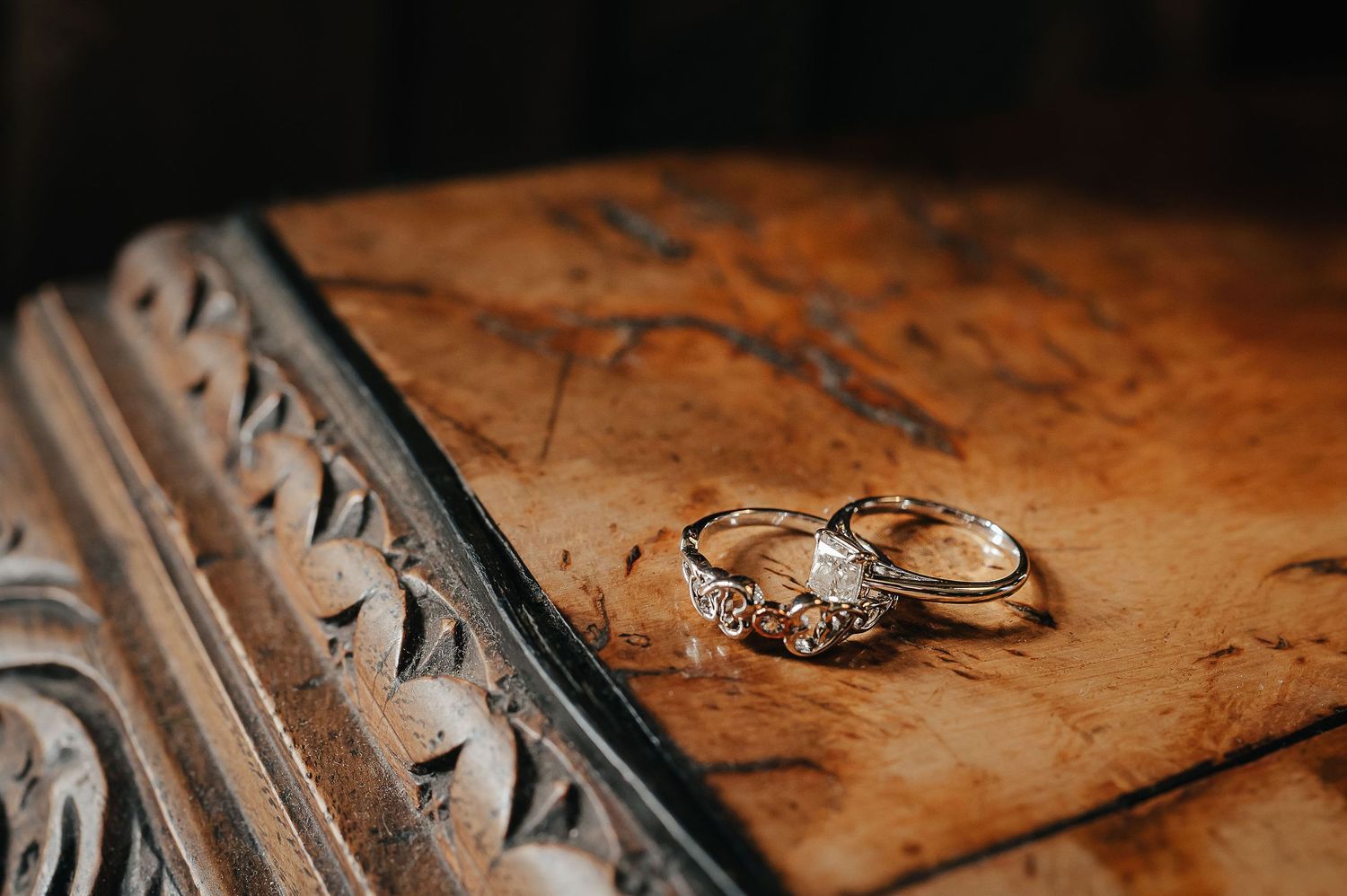 Wedding rings displayed on an ornately carved wooden surface in warm lighting.
