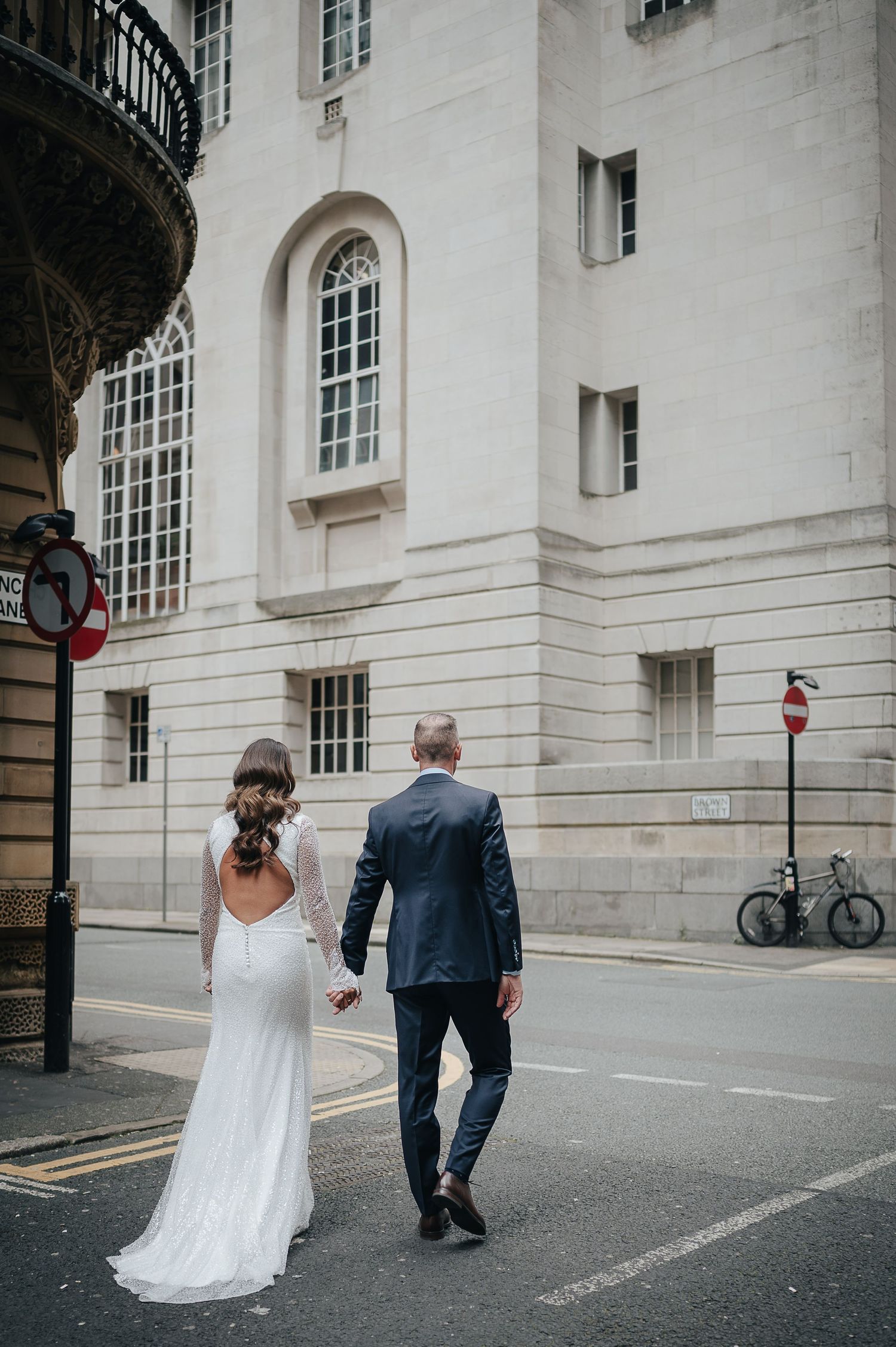 Newlyweds walking hand in hand down city street with classical architecture.