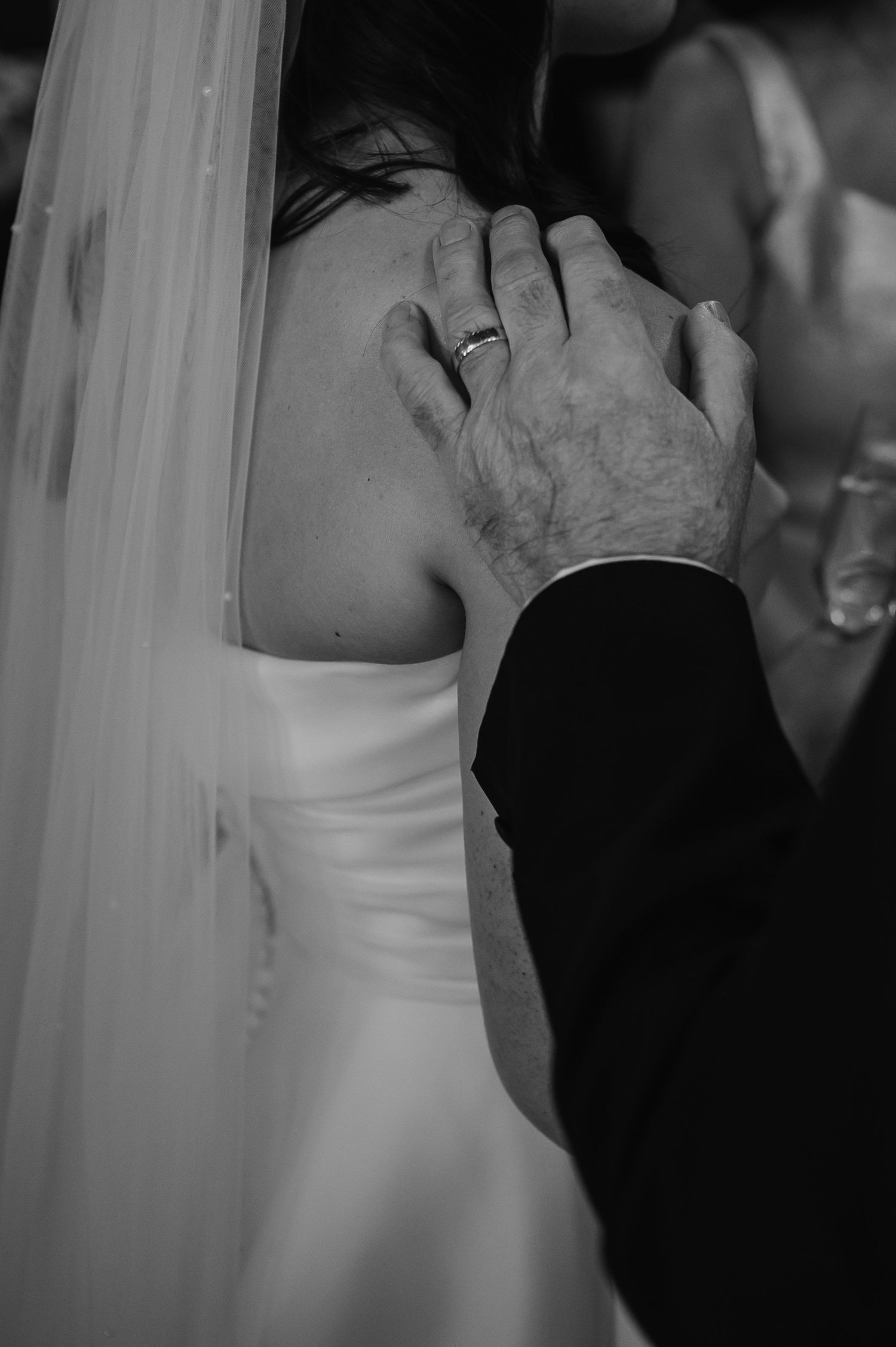 Black and white close-up of tender moment showing wedding ring detail.