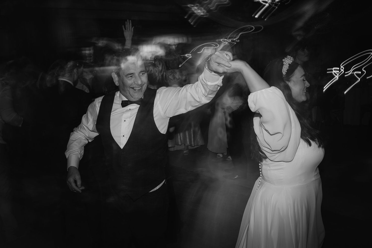 Couple dancing energetically at wedding reception in black and white.