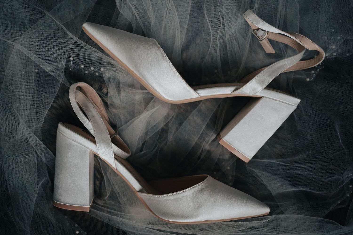 White wedding heels with block heel displayed on dark tulle fabric.