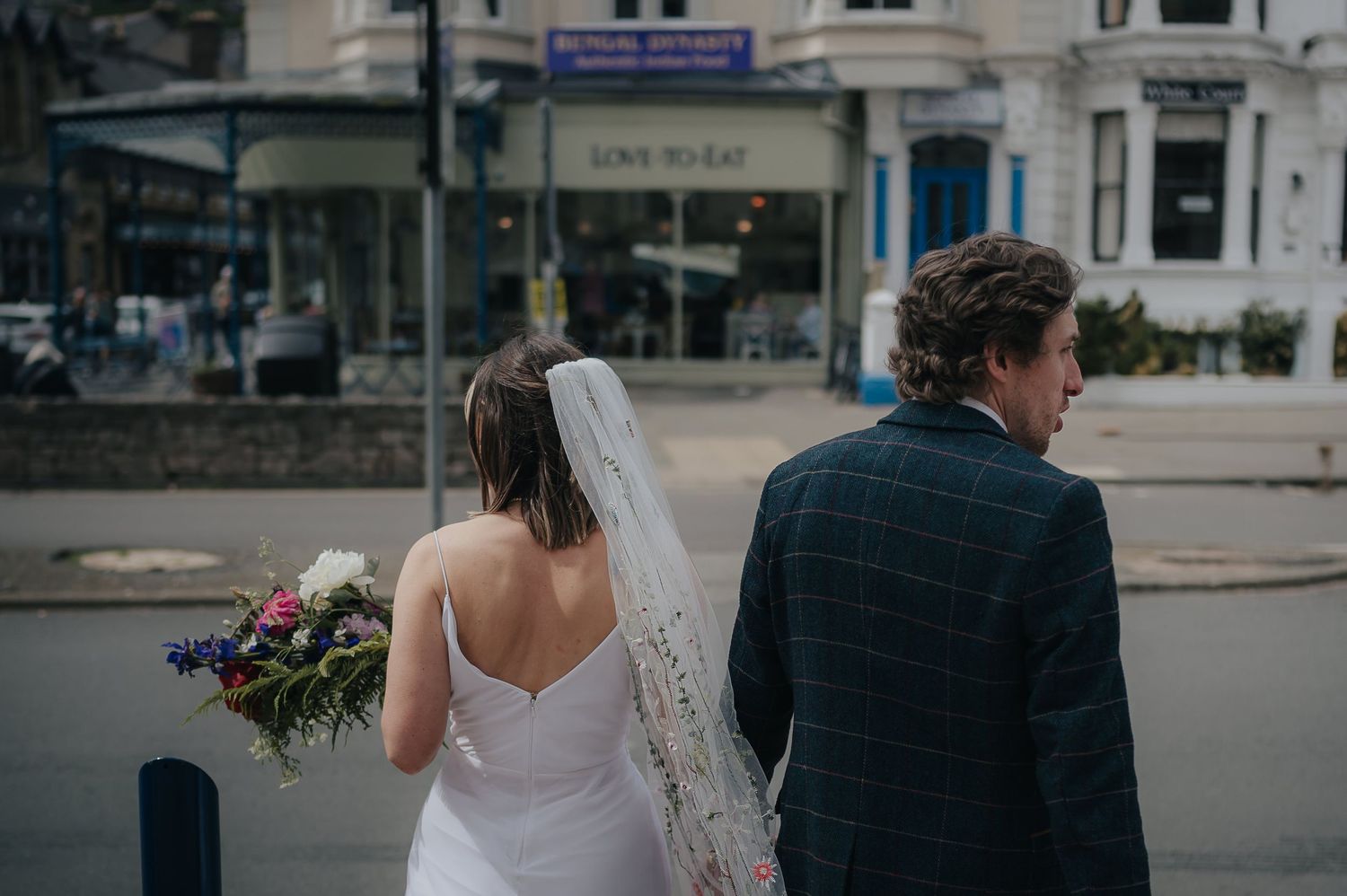 Wedding couple walking down a city street with the bride holding a vibrant floral bouquet.